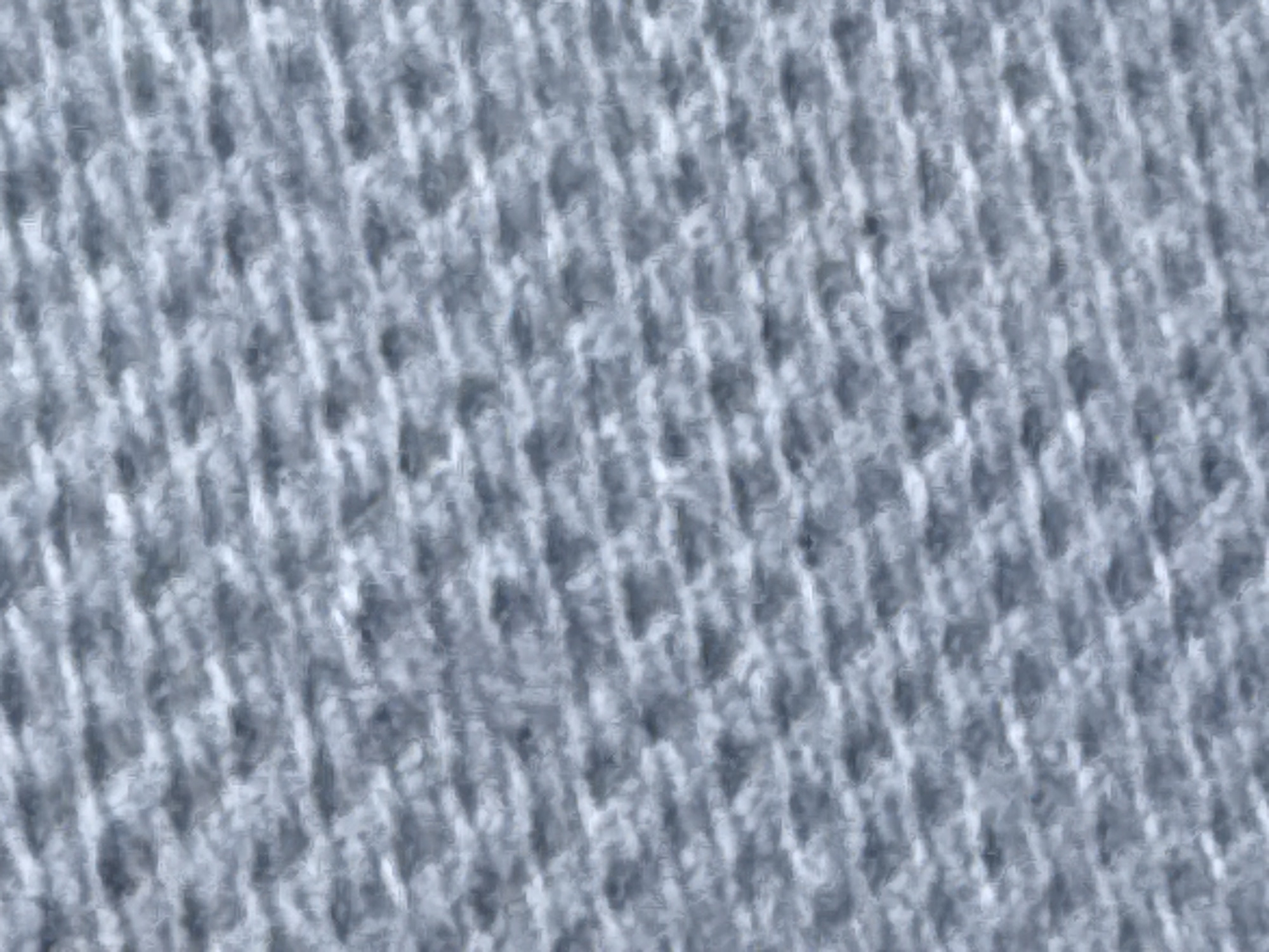 The image is a close-up, abstract shot of a textured fabric, likely a knitted or woven material. It is predominantly gray with lighter and darker variations creating a subtle pattern of horizontal and diagonal lines. The texture is coarse and appears to be made of intertwined fibers. There are no people, objects, or identifiable locations visible in the image. The image does not provide any information about Varna, Bulgaria, or any urban environment.