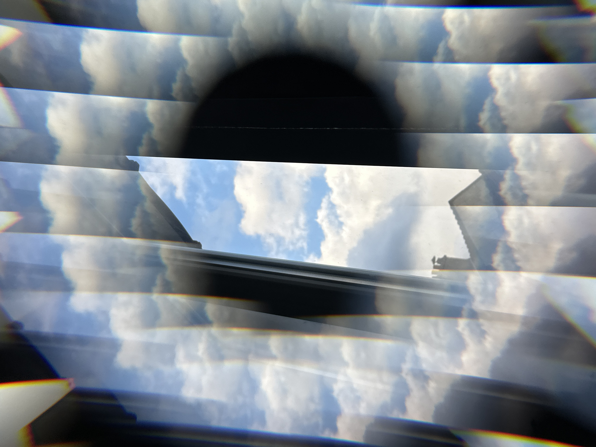 The image shows a view of the sky with clouds and parts of buildings, seen through what appears to be a prism or fractured glass. The repetition of elements suggests a multi-faceted perspective. Buildings are on the side of the image with a dark area.
It is hard to determine if the image is located in Palaiseau, France from the given picture.