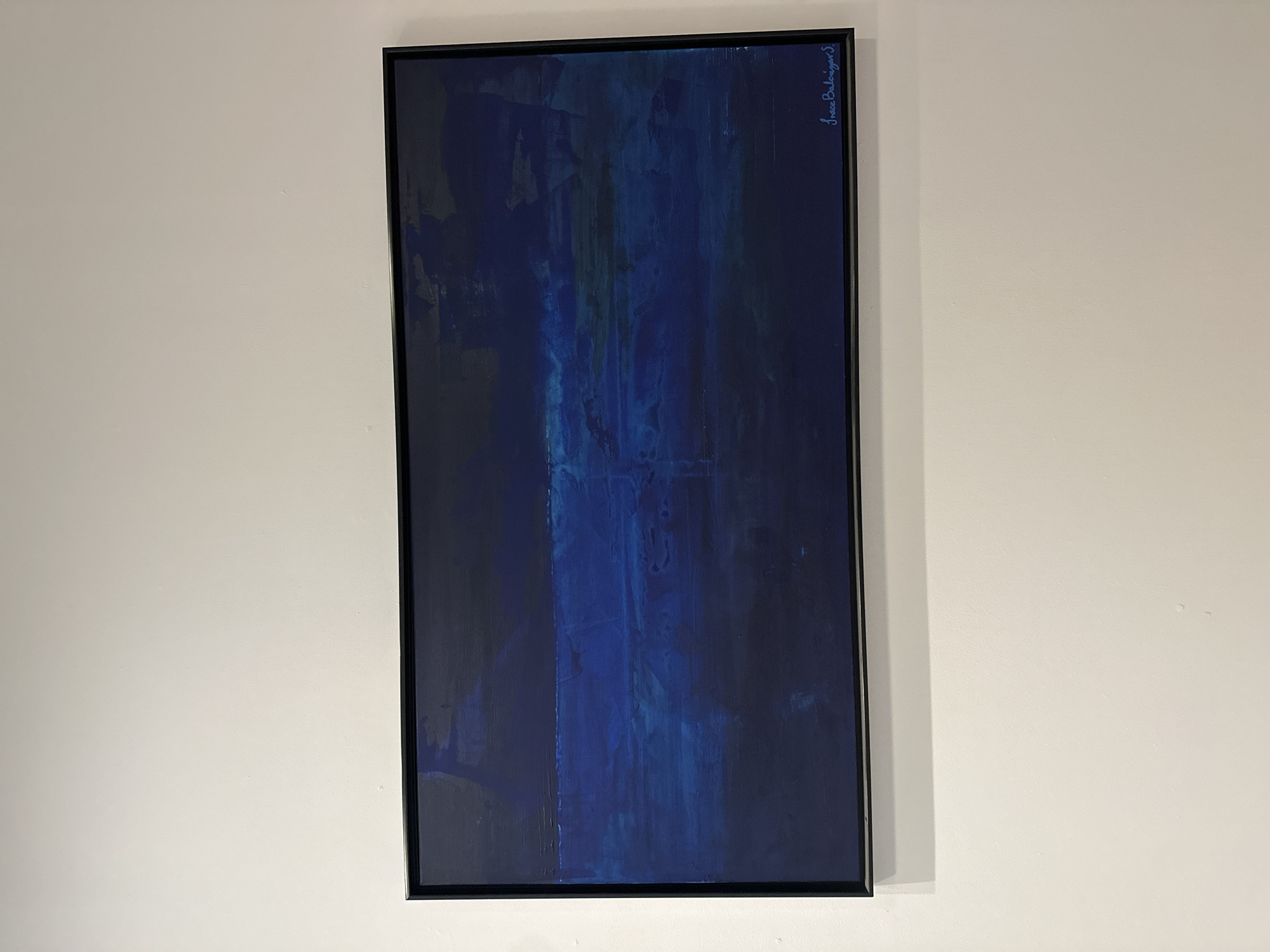 A framed painting hangs on a white wall. The painting is primarily blue and black, appearing abstract with vertical strokes. The frame is black. The signature "Jesse Barlagan S." is visible in the upper right corner of the painting. There is no discernible information to determine the location in San Bernardino Tlaxcalancingo, Mexico.