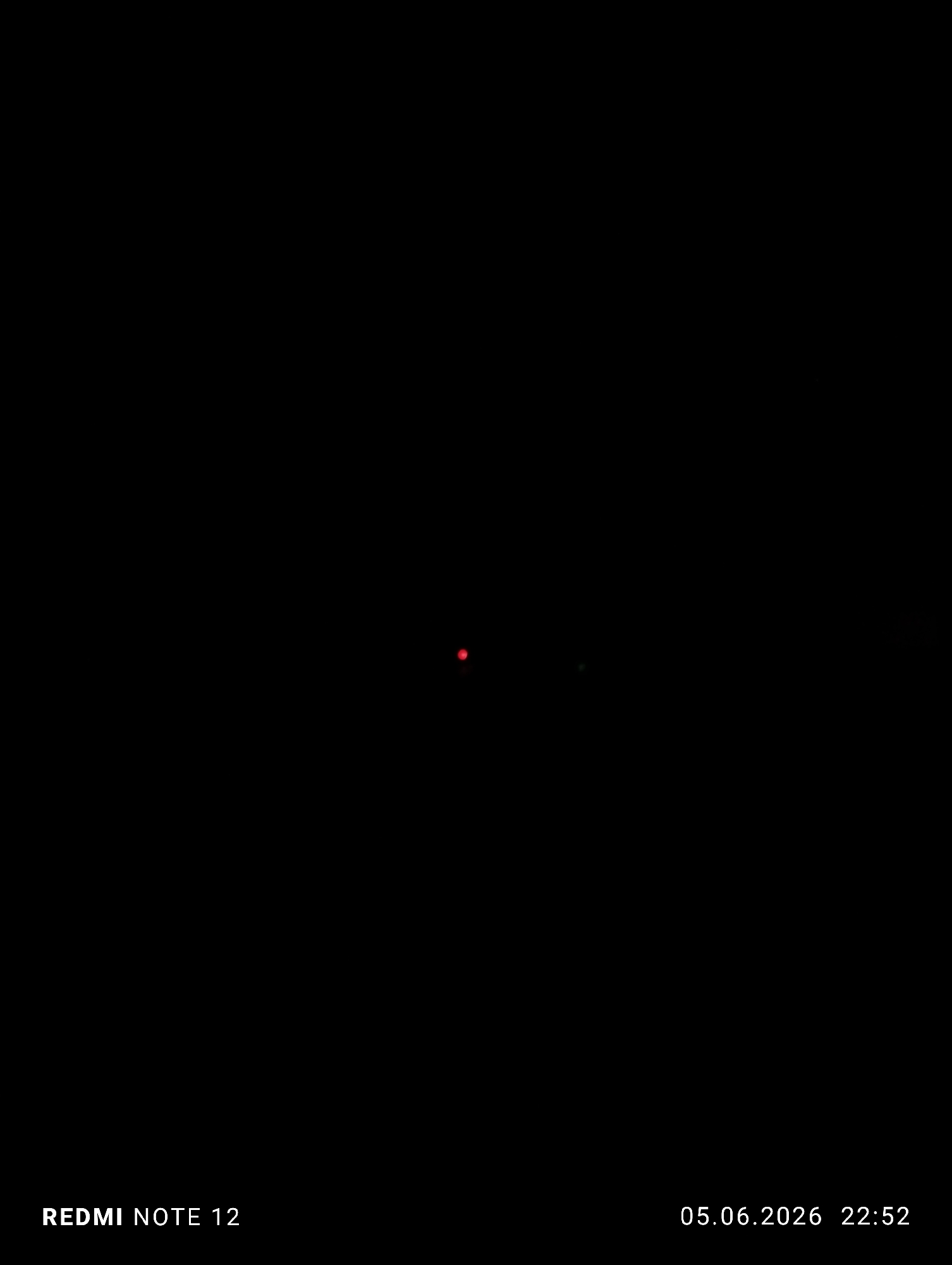 The image presents an almost entirely black frame, indicative of a very dark environment with minimal or no ambient light. Near the center, two small illuminated points are visible: a prominent red dot positioned slightly left of the vertical center, and a fainter green dot located to the right and slightly below the red dot. No other discernible subjects, objects, or environmental details are present within the dark expanse. White text overlays are visible in the lower corners. On the bottom-left, "REDMI NOTE 12" identifies the capturing device. On the bottom-right, "05.06.2026 22:52" provides the date and time of capture. The scene is located in Burgas, Bulgaria.
