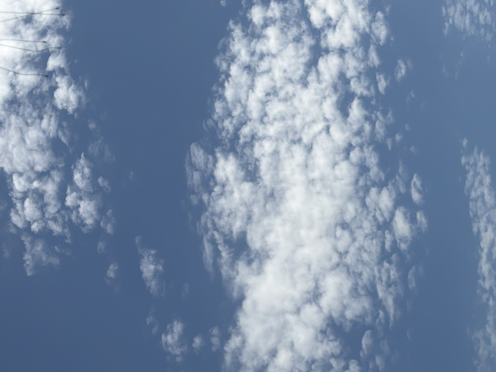 This media file depicts a clear blue sky with scattered white clouds. The clouds are diverse in size and shape, ranging from small, puffy cumulus clouds to larger, more wispy formations. The lighting suggests it is daytime, likely midday given the brightness of the sky and the stark contrast of the white clouds against the deep blue. There are no discernible people, objects, or text in the image. The scene is a natural skyscape, possibly taken from an elevated perspective or outdoors. No specific location cues are visible beyond the general sky and cloud formations.