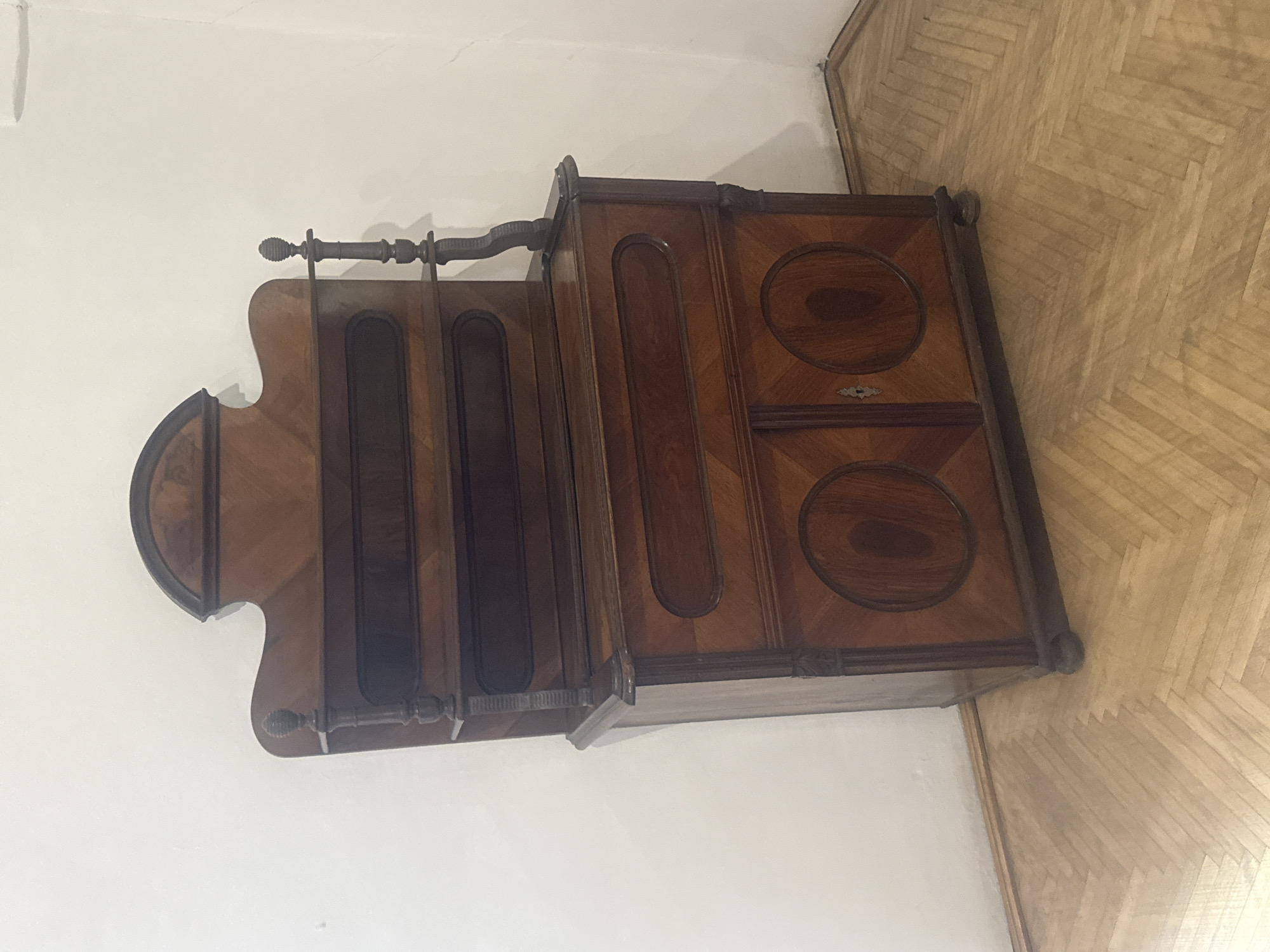 The image shows a brown wooden valet stand and cabinet against a white wall and parquet floor. The location is Unknown, Unknown.