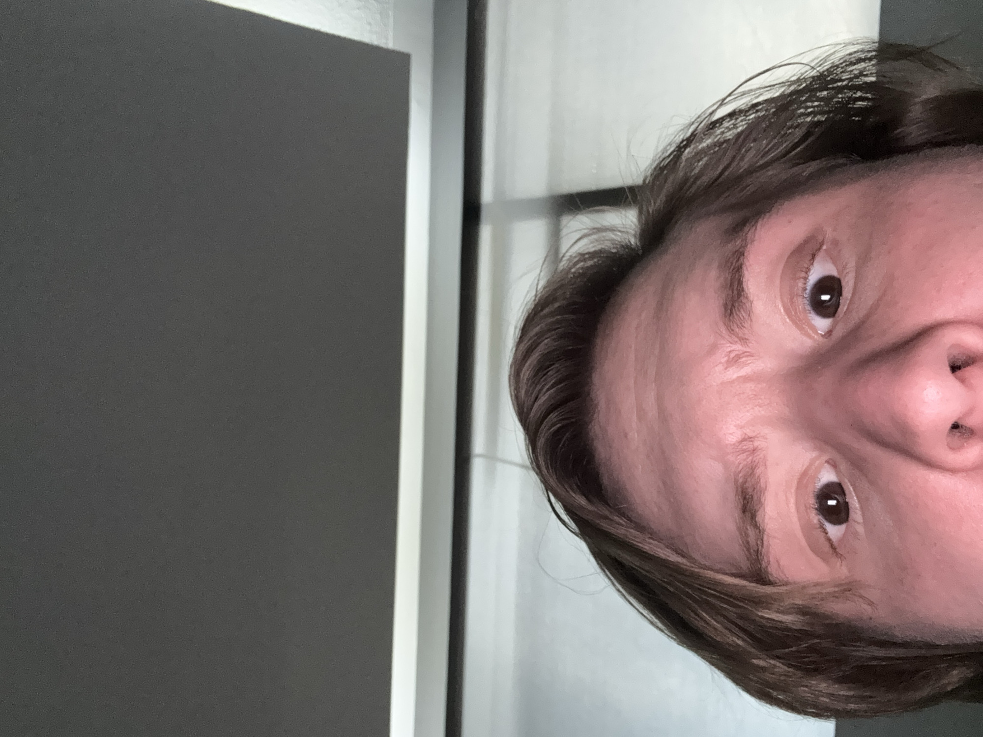 The image shows a close-up view of a person's face, angled to the right. The person has brown hair and brown eyes. The background consists of a gray wall on the left, with a white or light-colored wall and a window frame behind the person. No specific location within Cuautitlán Izcalli, Mexico, is identifiable from the given image.