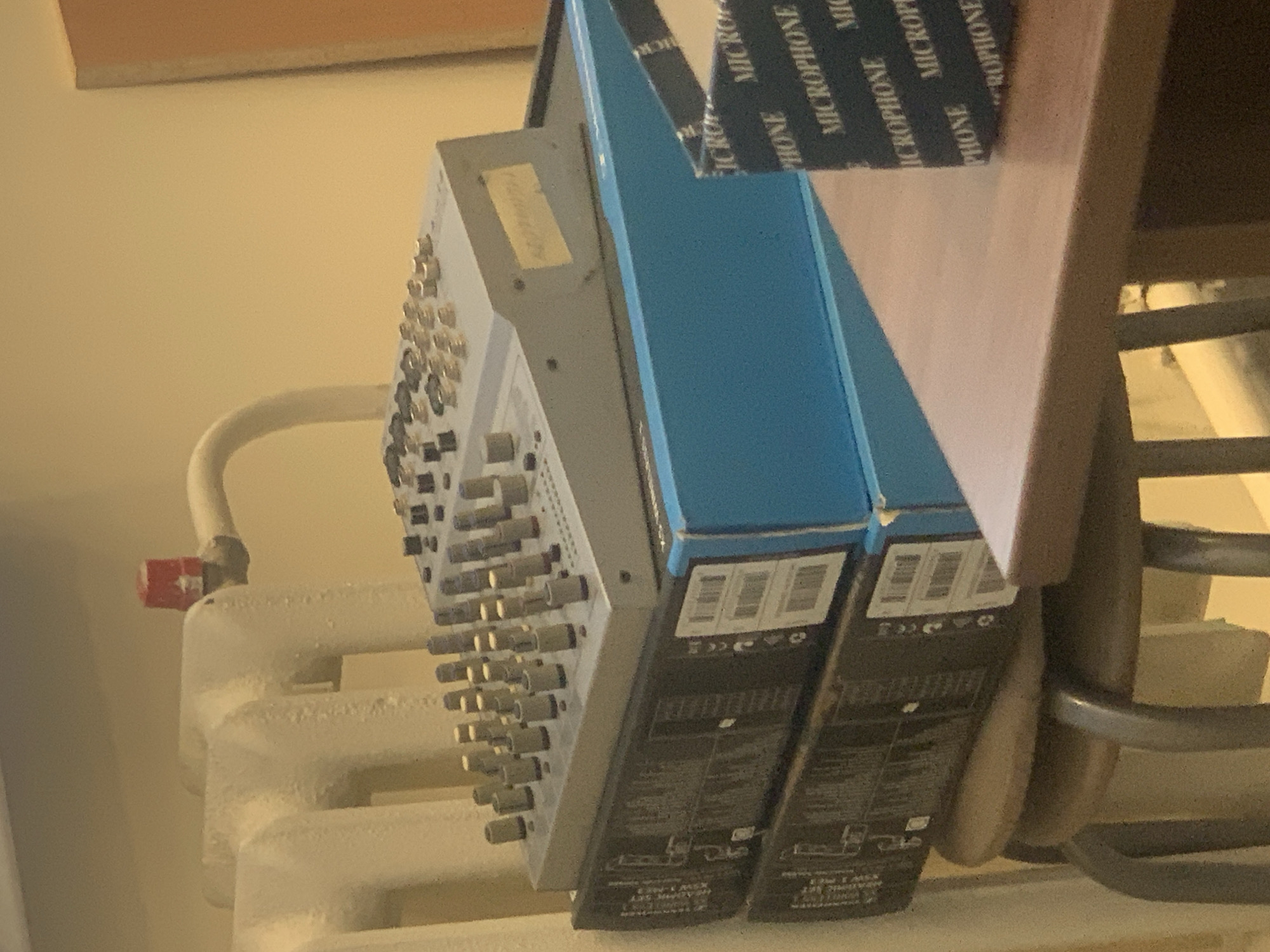 The image depicts two boxes labeled "Microphone" next to a mixing console, with the console appearing to rest on a white radiator. The setting is not specified or identifiable as being in Chaikovsky, Russia.