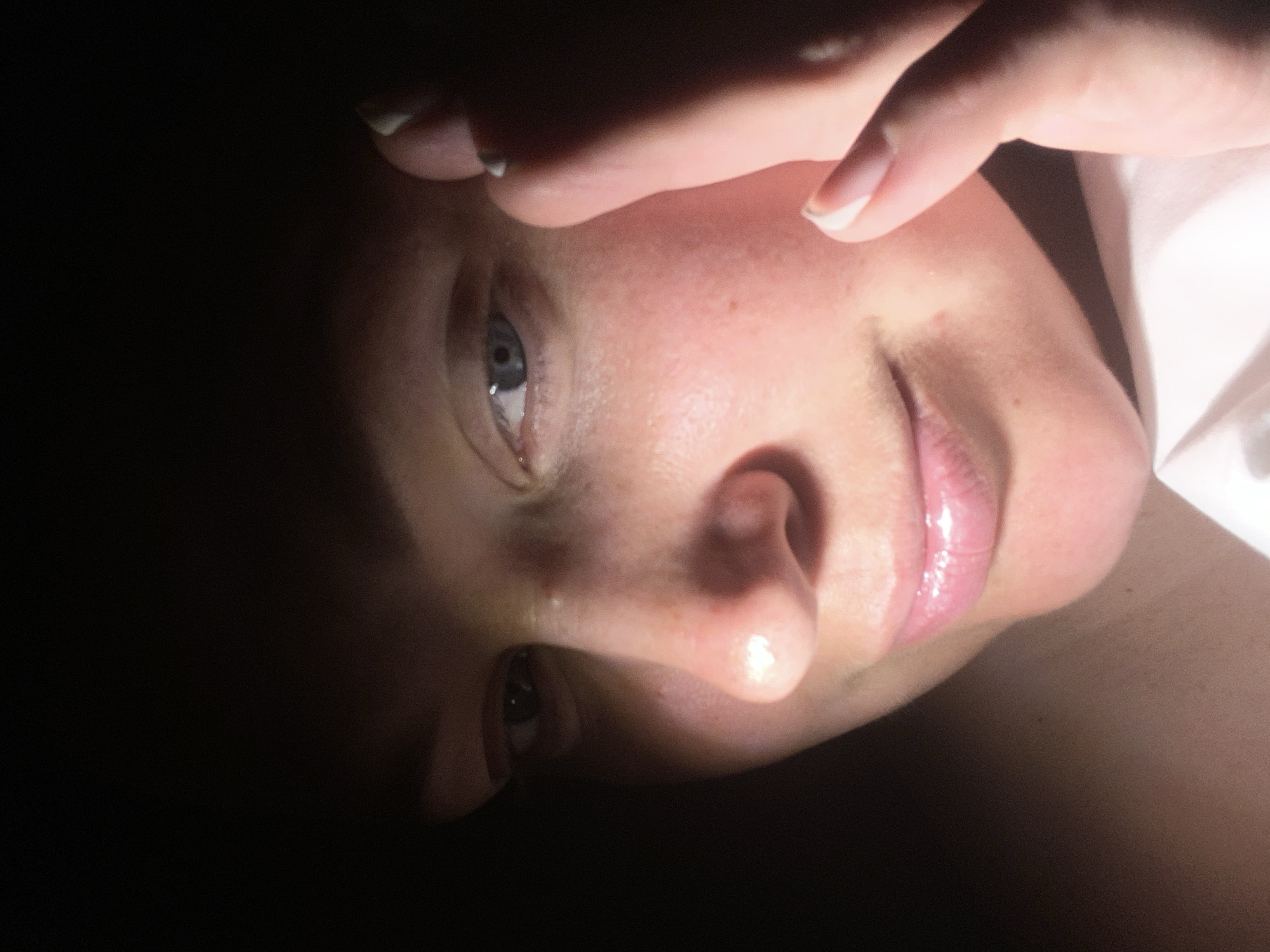 A close-up, angled view of a fair-skinned person's face, predominantly illuminated on the right side, while the left side is cast in deep shadow. The person's right eye is visible and light blue. Part of a hand is positioned near the top of the frame, partially obscuring the forehead. The nose and lips are prominent, with the lips appearing glossy. A white garment is partially visible on the right side of the image. The location in Sochi, Russia, is not discernible from the image.