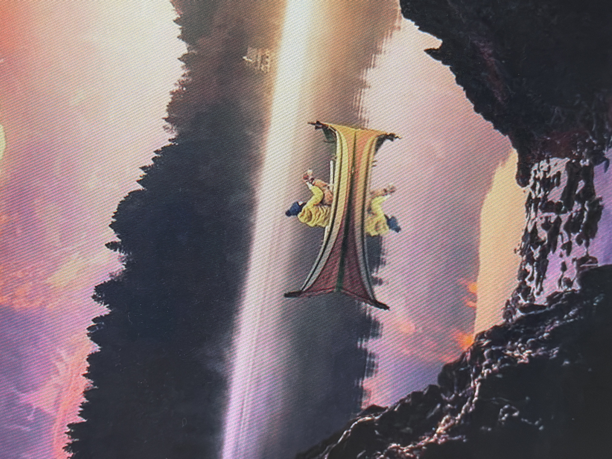 The image depicts a serene natural scene with a person in a boat on a misty lake at sunrise. The sky is painted with vibrant hues of pink and orange, reflecting on the calm water. Dense forests line the distant shore, shrouded in mist. In the foreground, rocky terrain adds a rugged element to the otherwise tranquil landscape. A person wearing a yellow jacket is seated in a small boat, holding what appears to be a fishing rod. The boat is gently drifting on the water, its reflection clearly visible. The overall atmosphere is peaceful and contemplative. There is no identifiable information that places this scene in the city of Homyel, Belarus.