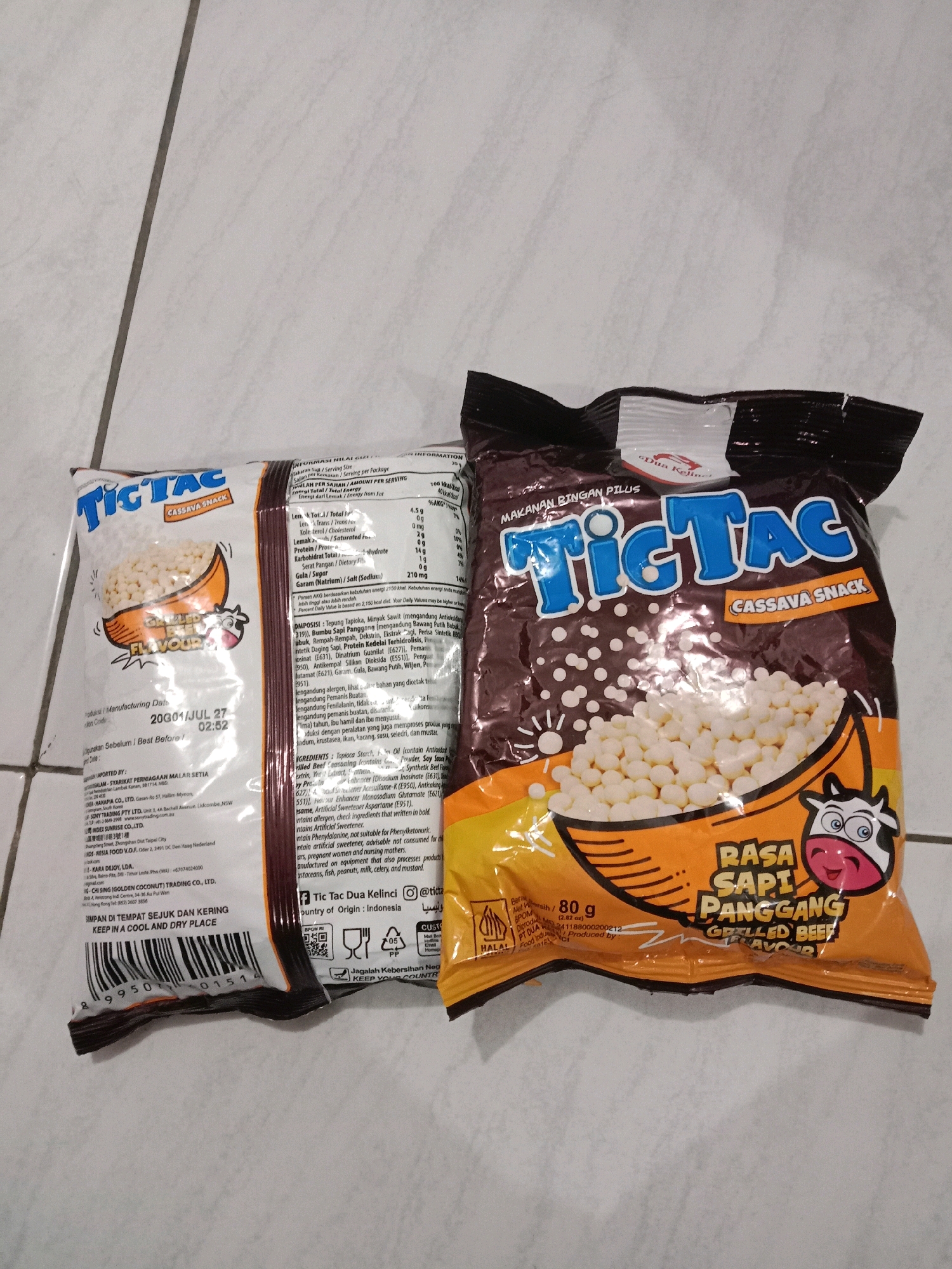 Two bags of Tic Tac snacks are displayed on a tiled surface. The bag on the left is partially obscured and features a "Gizzled Flavour" text. The bag on the right is fully visible and displays "RASA SAPI PANGGANG GRILLED BEEF FLAVOUR" in large, bold lettering. The tiled surface suggests an indoor environment, potentially a kitchen or a retail space. The image does not contain information about the city of Brangsong, Indonesia, nor any specific details regarding people, actions, or interactions.