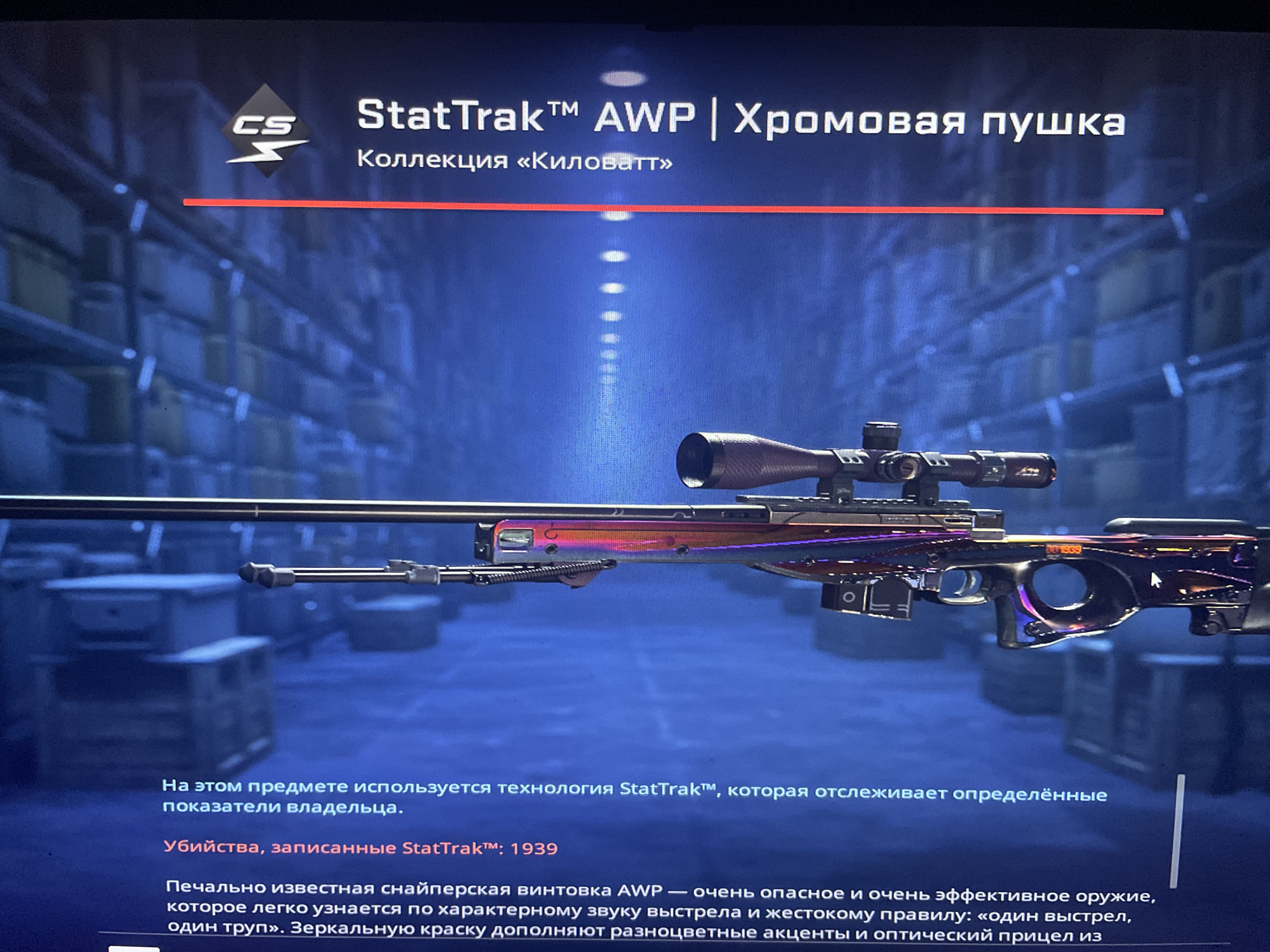 The image displays a close-up view of a weapon, specifically a sniper rifle, identified as "StatTrak™ AWP | Chromowa pushka". The weapon has a metallic, iridescent finish with purple, pink, and orange hues. It is positioned in the foreground, with a blurred background depicting shelves filled with boxes, suggesting an indoor storage or warehouse environment. Text overlays provide details about the weapon, including its designation and the presence of StatTrak™ technology for tracking kills. There is no information in the image that would allow for the determination of its location in the city of Kołobrzeg, Poland.