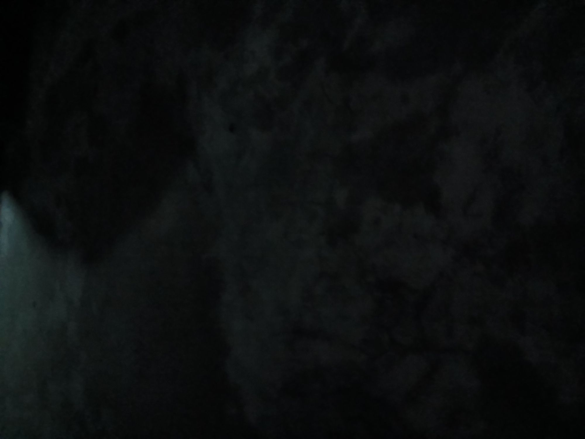 The image depicts a dark, textured surface, possibly a wall, with varying shades of black and gray. The uneven lighting creates a shadowy effect. The location in Lagos, Nigeria is not discernible from the image alone.