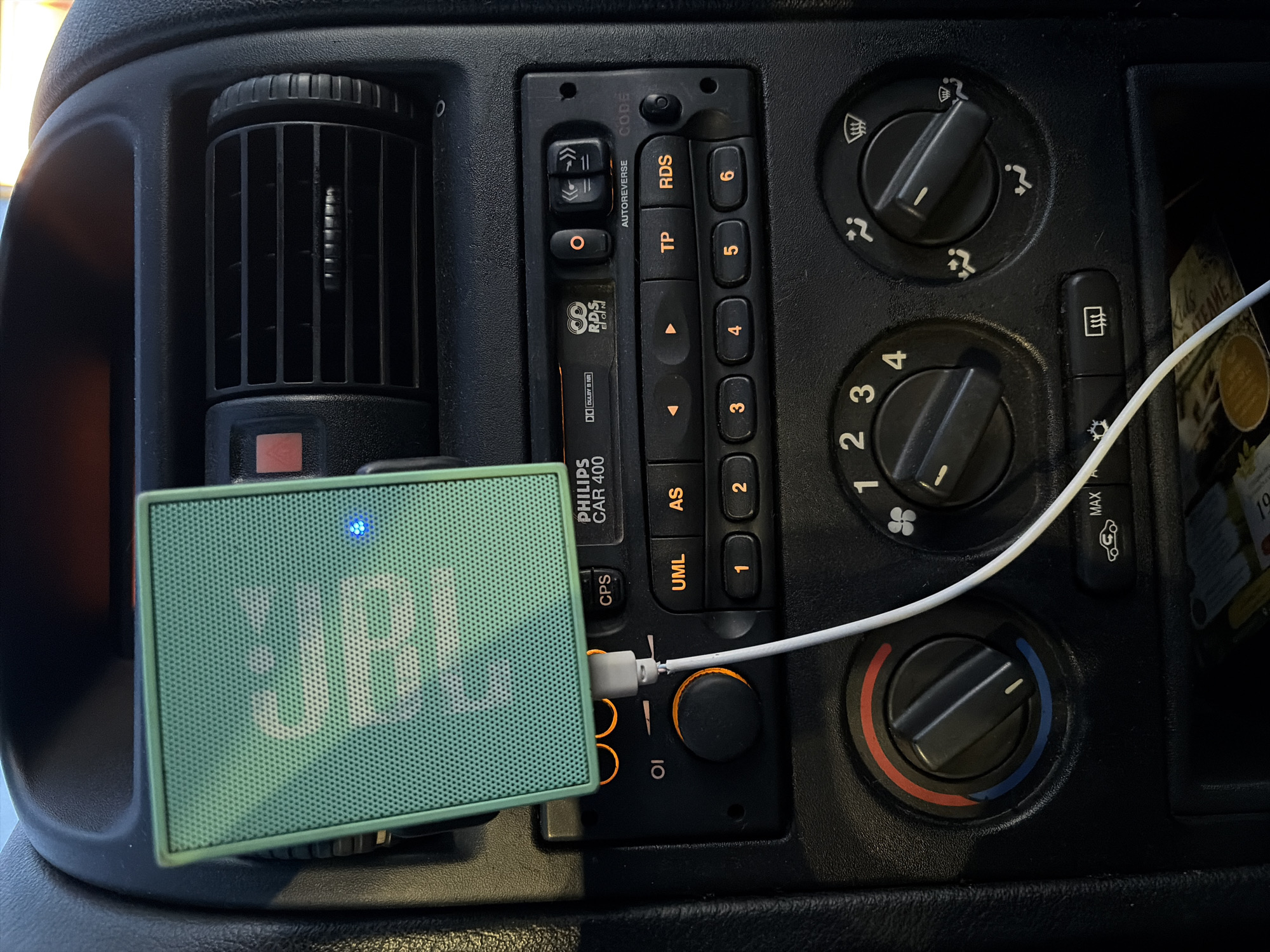 The image shows the dashboard of a vehicle. The dashboard is black and features a Philips CAR 400 car stereo, climate control knobs, and an air vent. A small, green JBL speaker is connected to the stereo with a white USB cable. The image does not contain information about Sofia, Bulgaria.