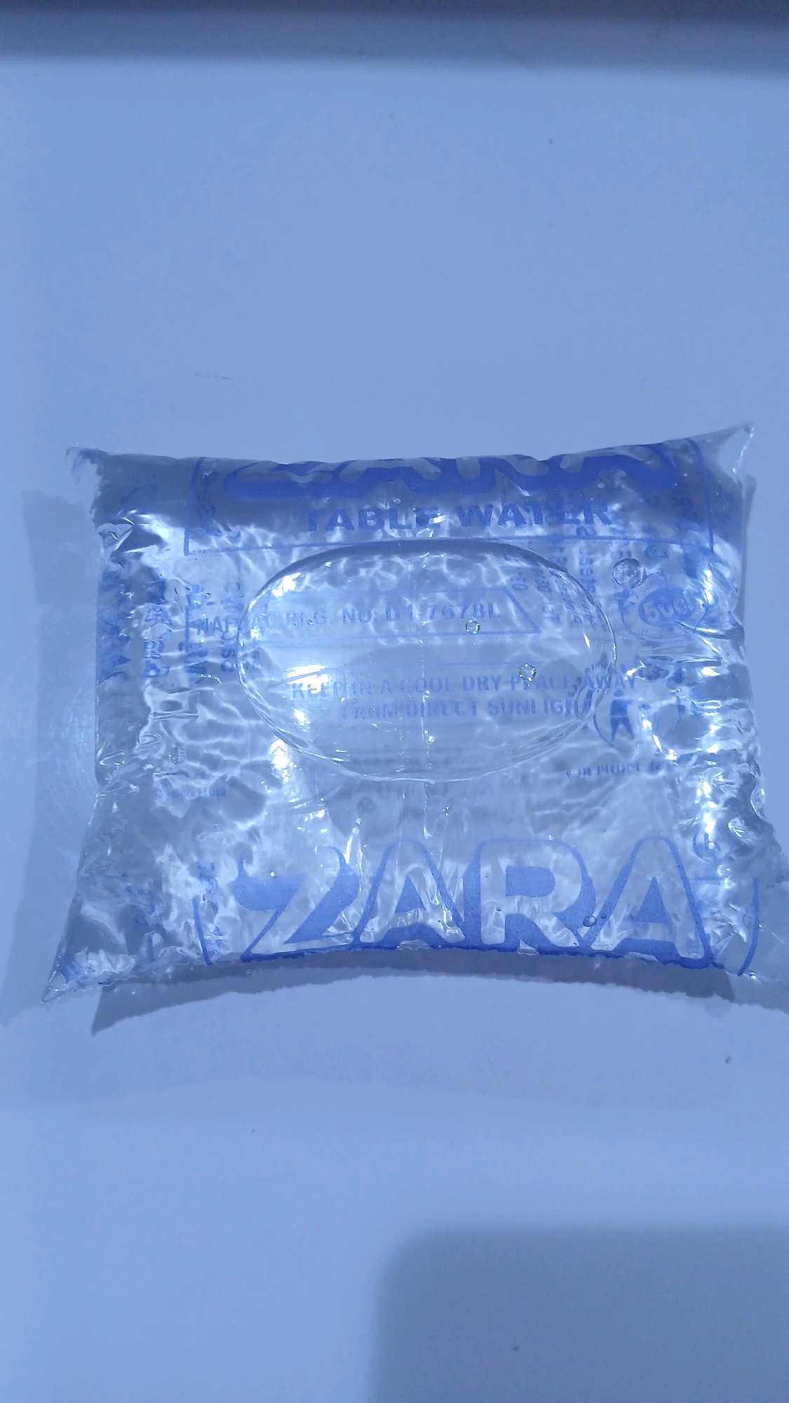 A sealed, clear plastic sachet of potable water is displayed against a light blue background. The sachet is rectangular with rounded corners and contains clear liquid. Blue text is printed on the sachet. The text at the top of the sachet reads "ABLE WATER", with the word "ABLE" partially obscured. In the center, an oval-shaped label has "REG. NO. D176781" printed on it, along with instructions to "KEEP IN A COOL DRY PLACE AWAY FROM DIRECT SUNLIGHT". The lower portion of the sachet features the brand name "ZARA" printed in large blue letters. The image does not provide any information about the city of Gura Top, Nigeria.