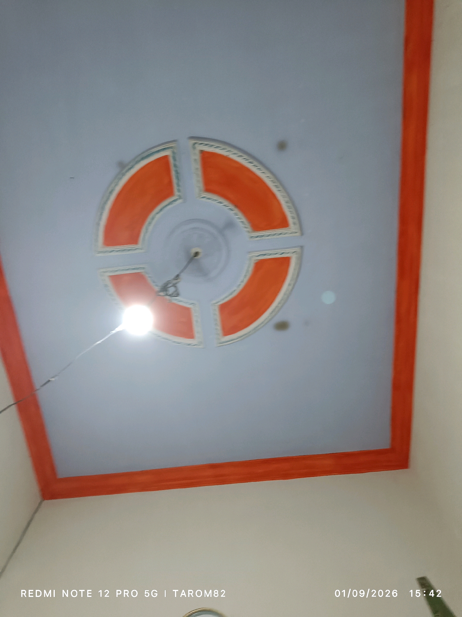 The image shows a ceiling with an orange and white decorative pattern. A bright light bulb is hanging from the ceiling by a wire. The text "REDMI NOTE 12 PRO 5G | TAROM82" and the date "01/09/2026 15:42" are visible at the bottom of the image, indicating it was taken with a Redmi Note 12 Pro 5G phone and that the location is likely Tarom82. Based on the available information, the location is not specified to be in Rejoagung, Indonesia.