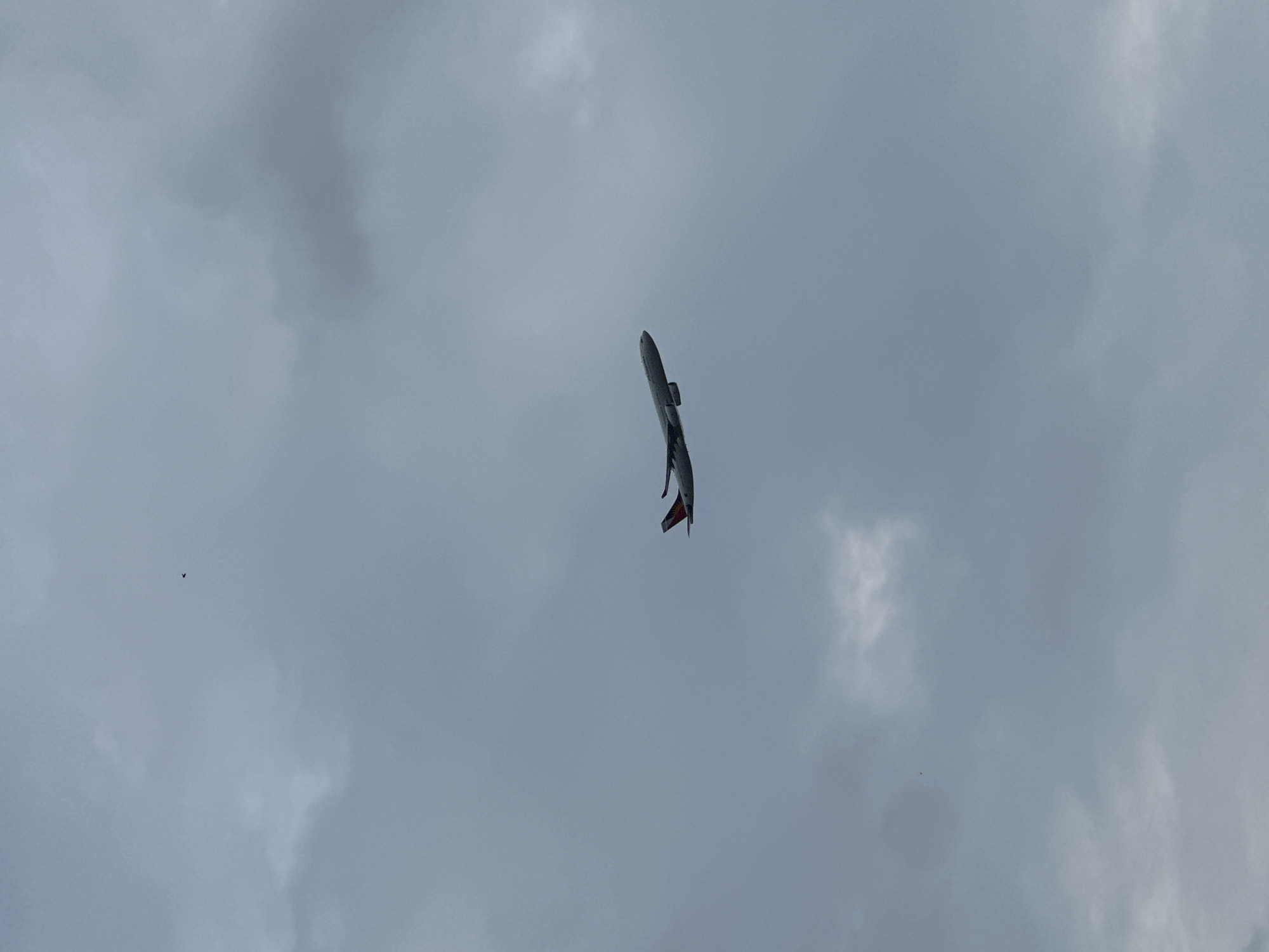 A commercial airplane is flying in a cloudy, gray sky. The tail of the plane is visible and is red and white.
