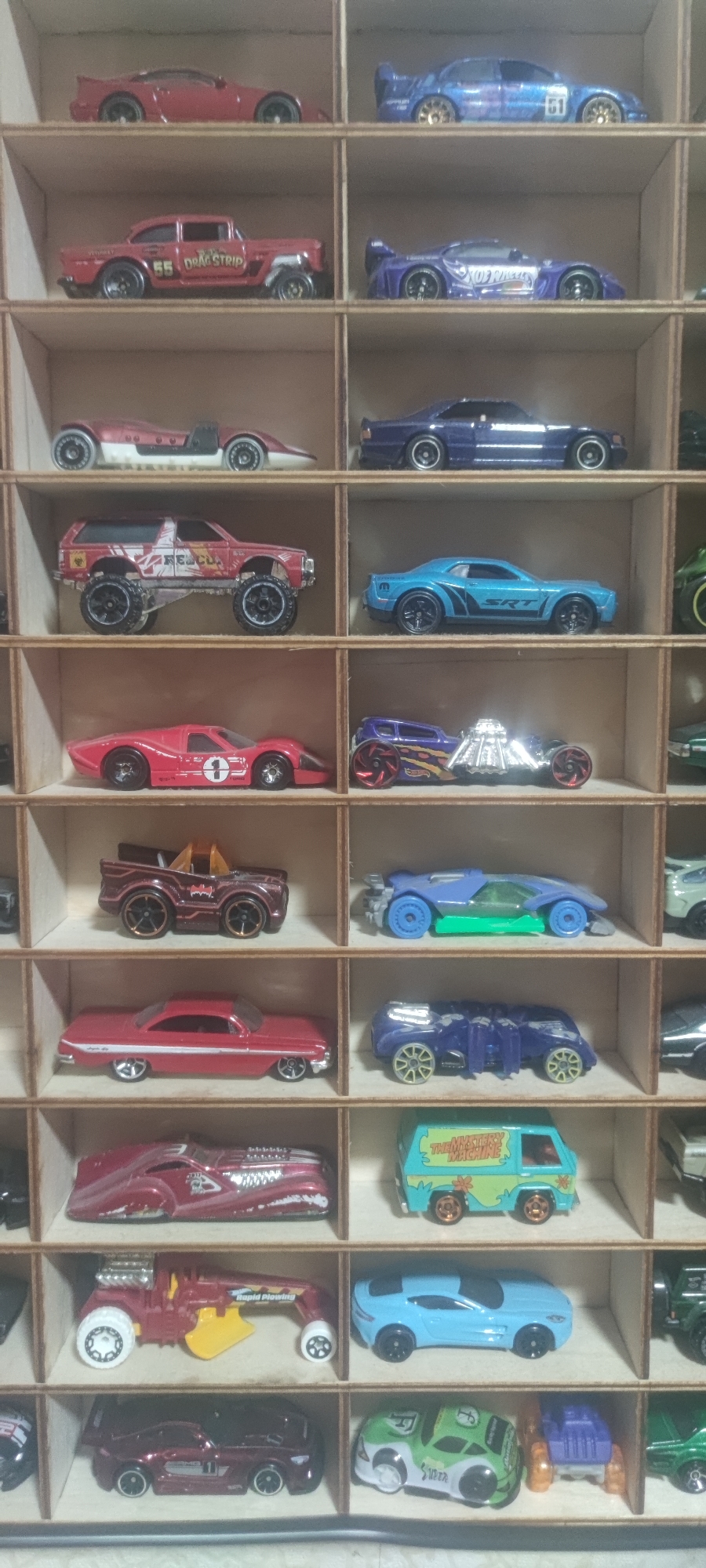 The image displays a grid of small, die-cast toy cars arranged in wooden compartments. The cars are of various colors and models, including sports cars, trucks, and vans. There are no people or any elements that indicate a specific location in Yakutsk, Russia. The environment is a neutral background, suggesting the toys are part of a collection or display.
