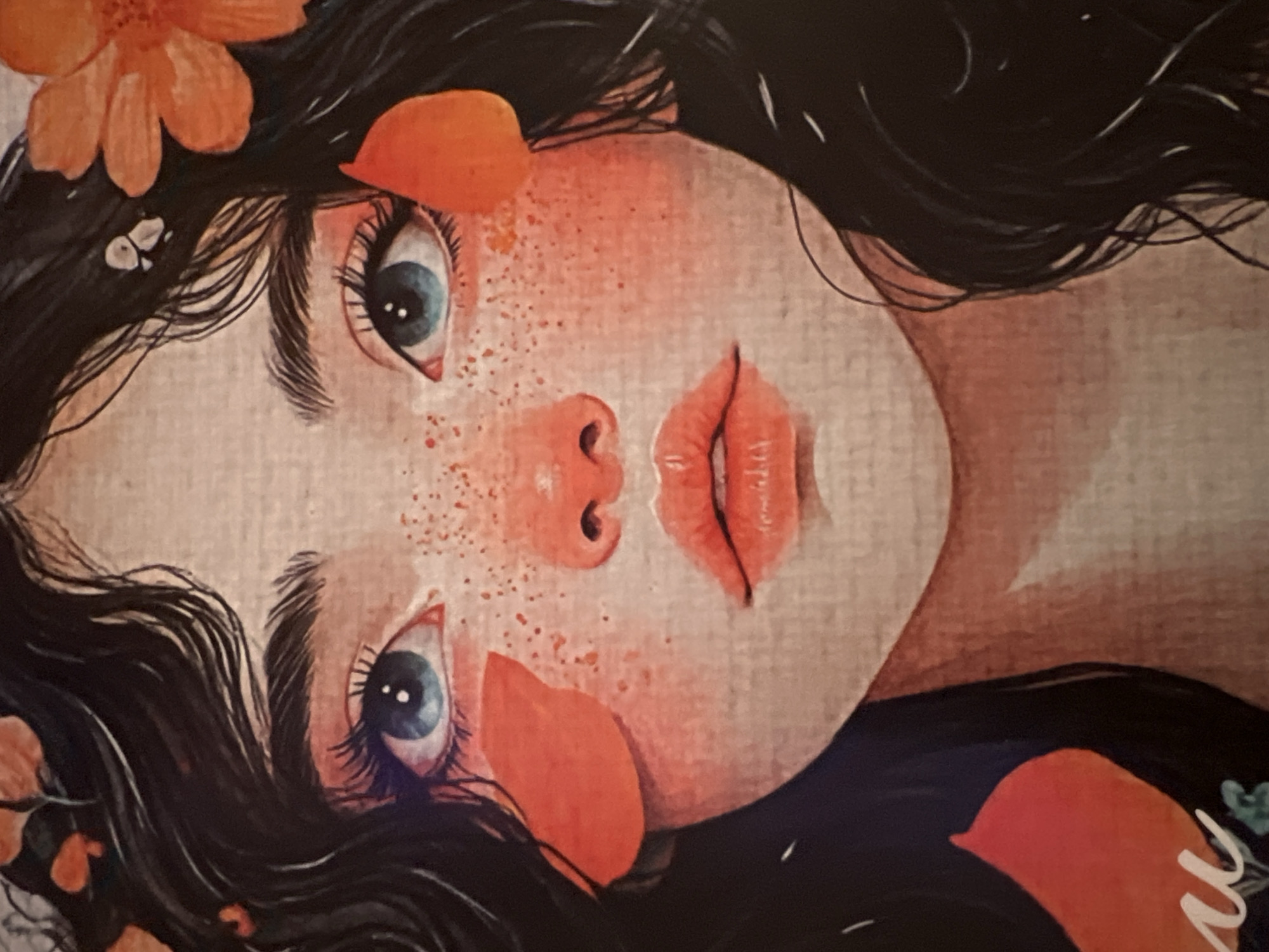 This is a close-up, artistically rendered illustration of a young person's face, tilted to the side and viewed from a low angle. The subject has long, dark, wavy hair adorned with several orange flower petals. Their skin is fair and dotted with numerous small, reddish-brown freckles, particularly on the cheeks and across the bridge of the nose.
The subject has striking blue eyes with long, dark eyelashes. The eyes are open and appear to be looking towards the viewer. The nose is small and delicate, and the lips are full, parted slightly, and painted a vibrant orange-red color. Reddish-orange petal shapes are strategically placed on the face, one near the left eye and another on the cheek.
The overall mood of the illustration is gentle and perhaps a bit melancholic or dreamy, evoked by the soft lighting, the muted color palette with pops of orange, and the subject's serene expression. The background is a textured, light-colored surface, possibly representing canvas or paper, with soft shading that hints at a subtle, warm-toned environment. There is no clear indication of a specific time of day, weather conditions, or a definable location beyond the general artistic setting. No visible text is present in the image.