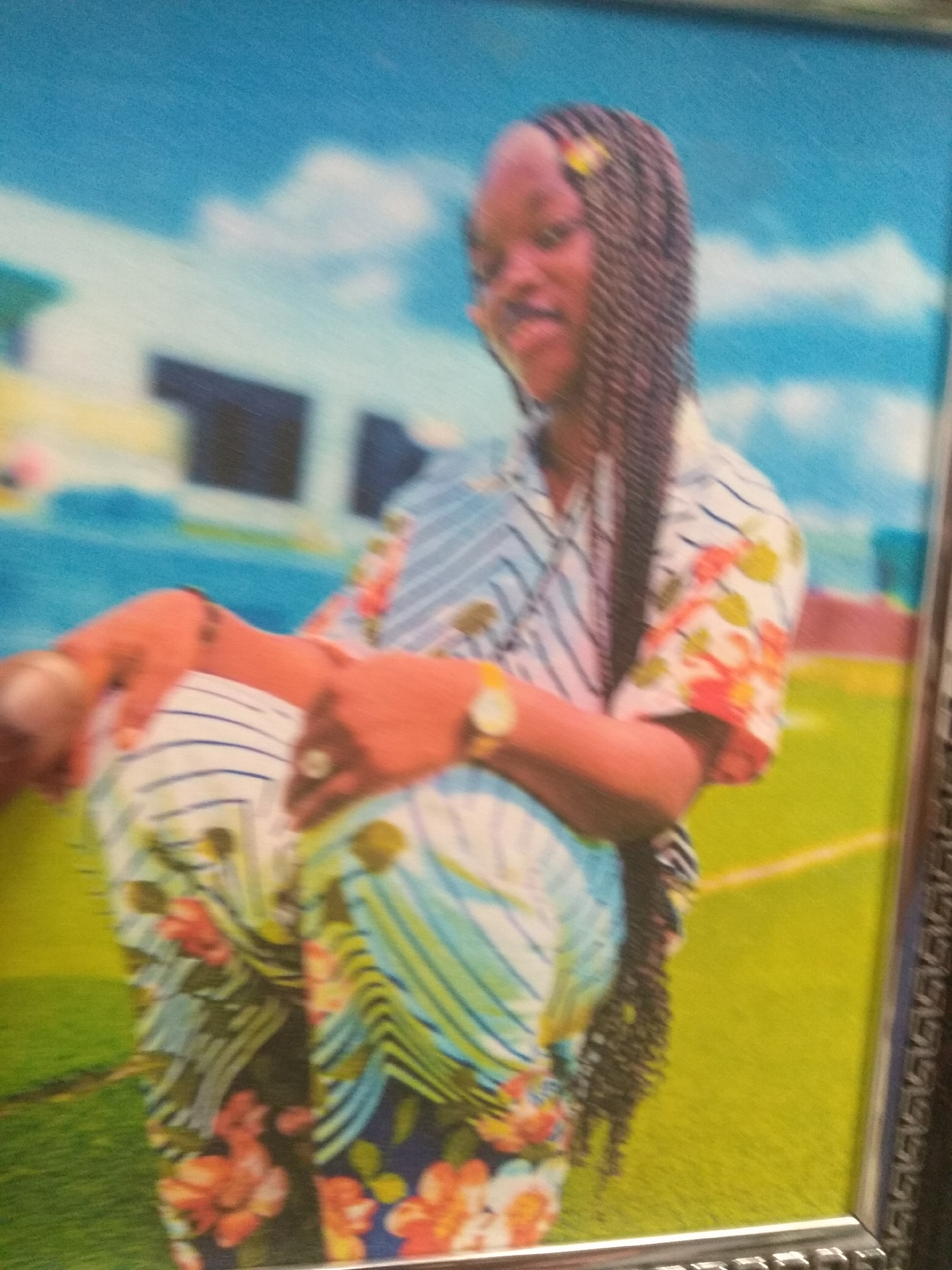 The image depicts a framed portrait of a young Black female. She is shown in a seated or reclining pose, with her body angled to the right. Her hair is styled in long, dark braids, with a small yellow accessory visible. She is wearing a colorful, patterned outfit with floral motifs and stripes. Her right arm is bent, with her hand resting on her lap, and she appears to be wearing a watch on her wrist.
The background of the portrait is a blur of blues and greens, suggesting an outdoor setting with a sky and some form of vegetation or open ground. The image is a photograph that has been framed, with a decorative border visible on the right and bottom edges. The lighting suggests a slightly overcast day or an indoor setting with diffused light. The overall impression is that of a posed portrait for display.
The question asks for the location in the city of Jalingo, Nigeria. However, the image itself does not contain any explicit visual cues that would allow for the identification of a specific location within Jalingo, Nigeria. There are no landmarks, signs, or environmental features that are uniquely characteristic of that city. Therefore, I cannot provide details about the location.