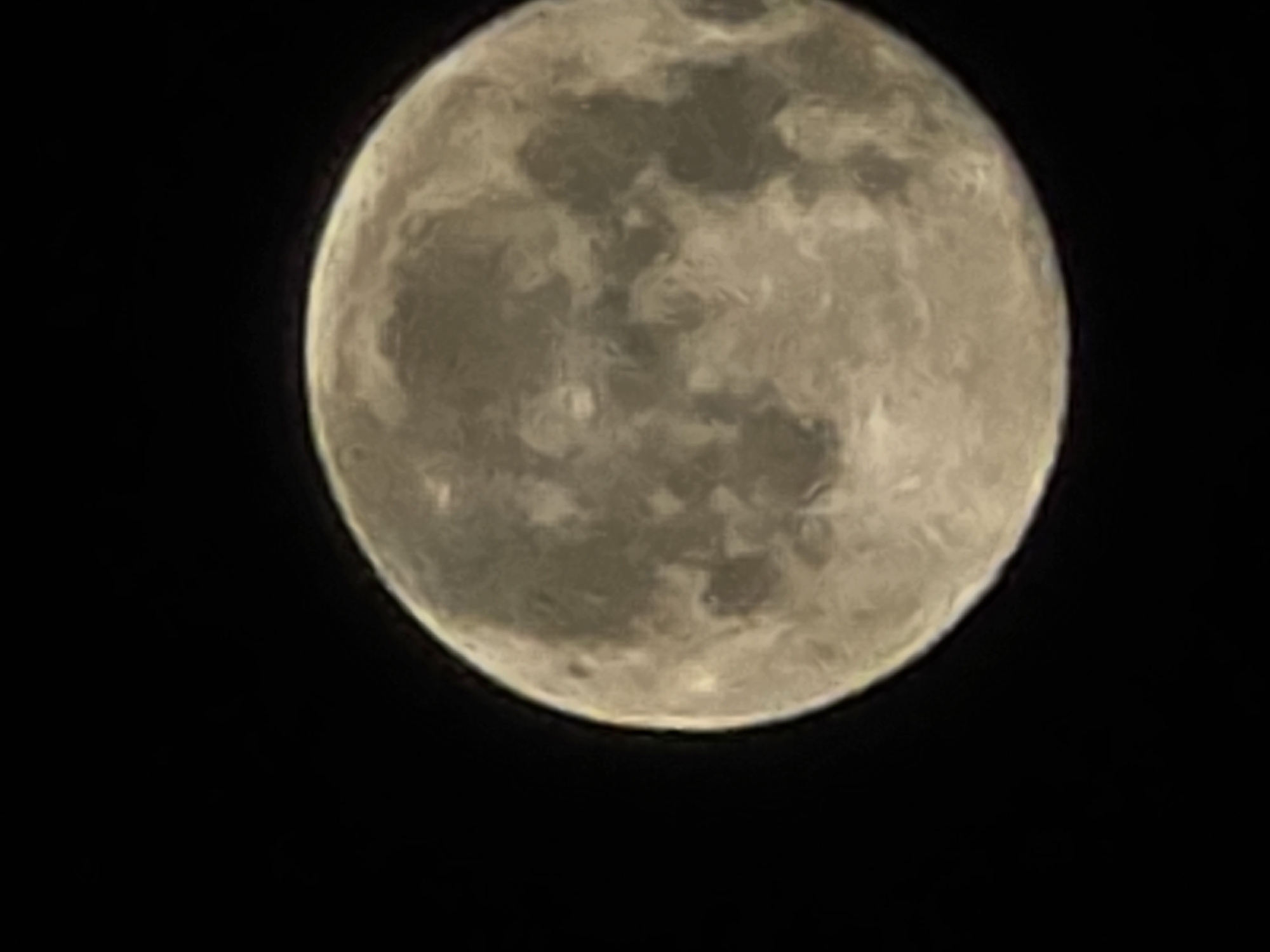 The image is a close-up, slightly out-of-focus photograph of the full moon against a black sky. The moon's surface is visible, with its characteristic craters and maria, appearing in shades of grey, beige, and white. The lighting suggests it is illuminated by the sun from an unseen angle. There are no other objects or discernible features in the image. This image does not contain any information related to the city of Yambol, Bulgaria, or any urban environment.