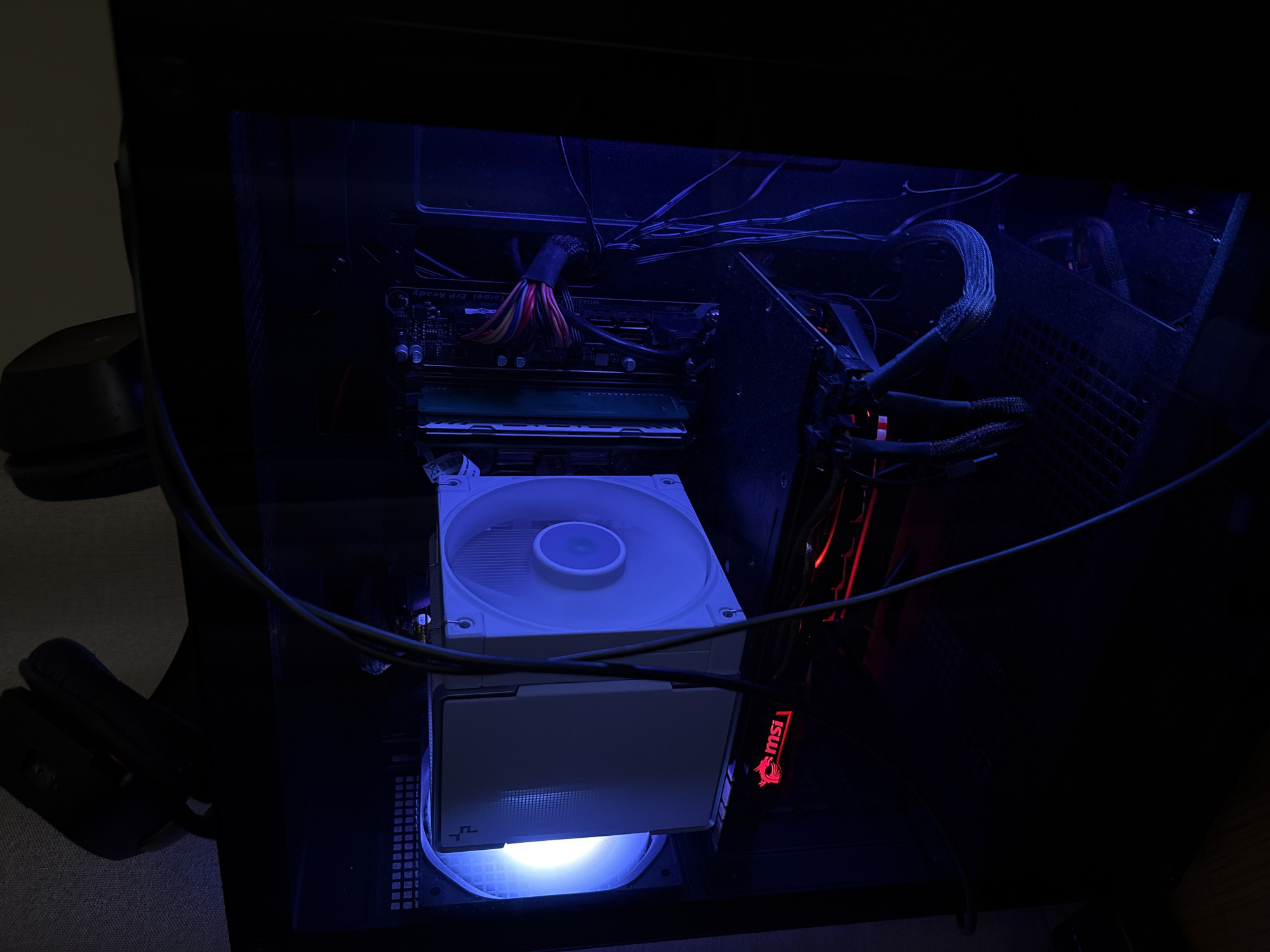 The image shows the interior of a computer case illuminated with blue and red LED lights. Inside, components such as RAM modules, a white CPU cooler, and a graphics card with an MSI logo are visible. Cables are routed across the top of the case. The location is not discernible from the image.
