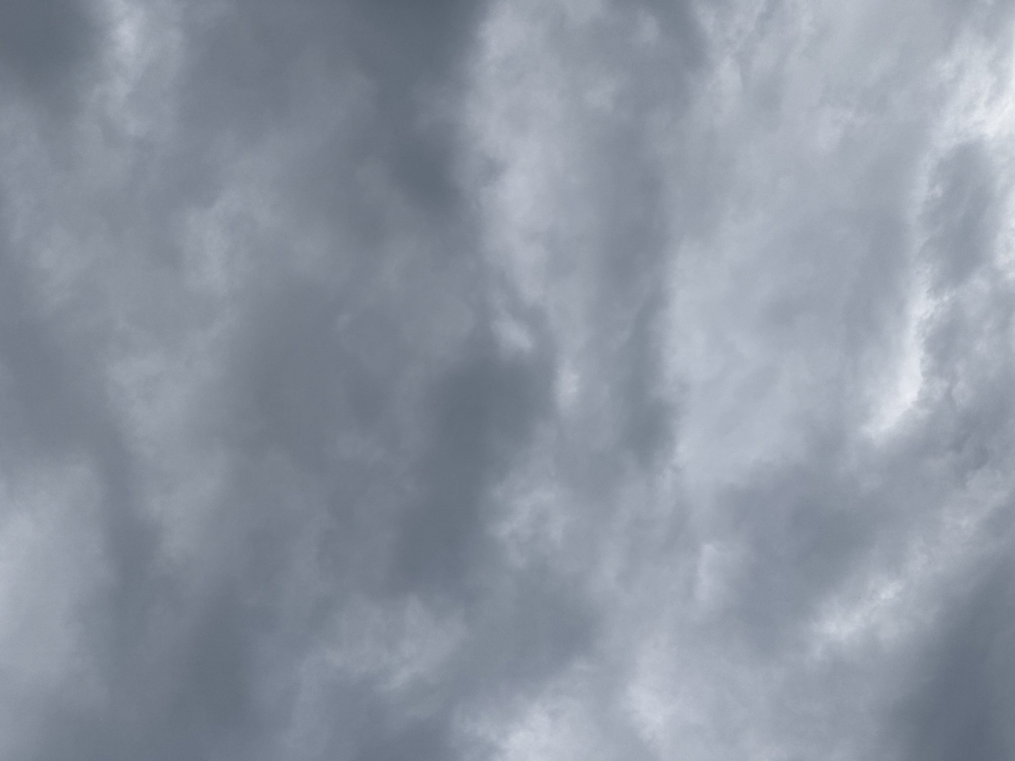 The image is a full-frame, eye-level, outdoor photograph of a cloudy sky. The clouds are dense and dark gray, suggesting an overcast or stormy weather condition. There are no discernable landmarks, people, or objects within the frame. The lighting is diffused and even, characteristic of a heavily clouded sky. The scene appears to be a generic view of the sky, without specific visual cues to pinpoint its location within Kremenchuk, Ukraine, or any other city. The composition is abstract, focusing solely on the texture and tonal variations of the clouds.