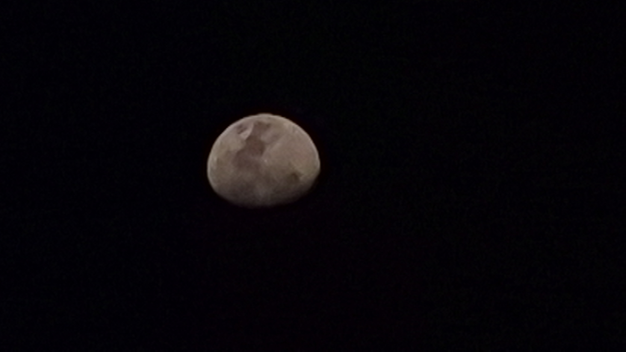 A crescent moon is visible against a black sky. The moon is illuminated on its right side, showing surface details such as craters and maria. The rest of the moon is in shadow.