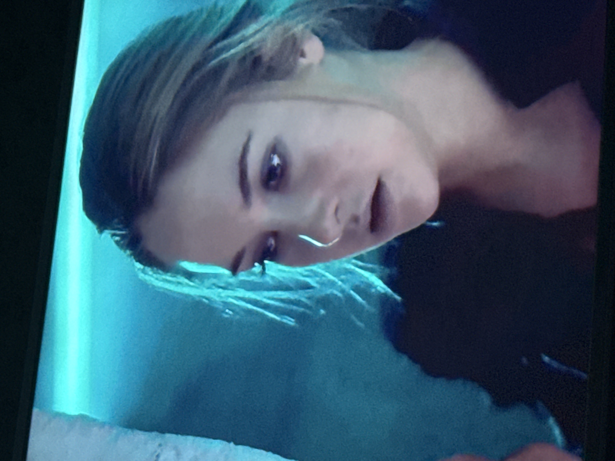 A close-up shot depicts a fair-skinned young woman with dark eyes and light brown hair. She has a nose ring. The background is a blurry mix of teal and darker hues. There is no indication of a location in Mytishchi, Russia.