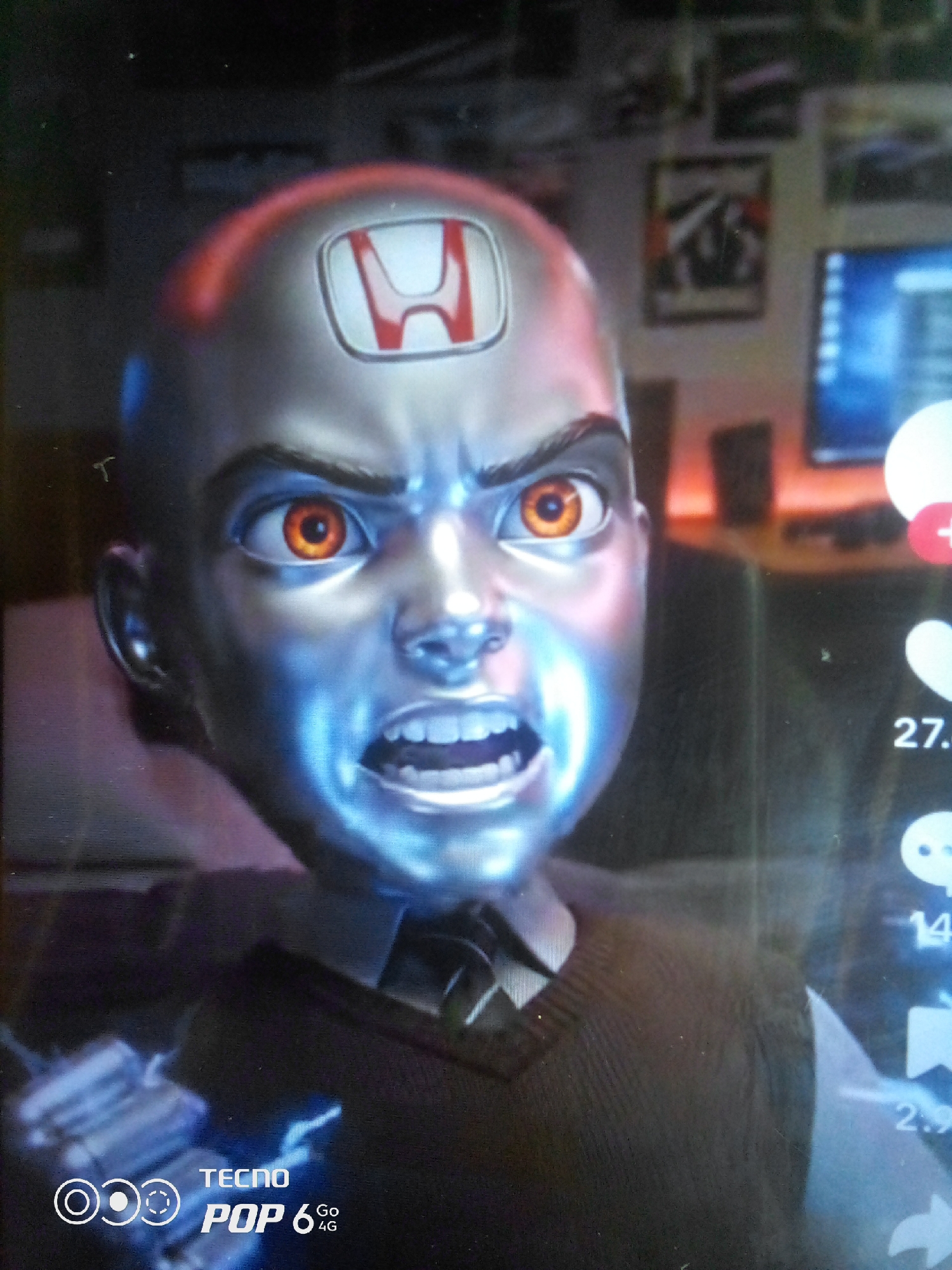 This is a close-up, low-angle, vertical medium shot of a CGI character's head and shoulders. The character has a metallic, silver-toned skin with bright orange, glowing eyes and an angry expression. A red and white Honda logo is prominently displayed on its forehead. The character is wearing a dark vest over a white shirt with a dark tie. The background is out of focus, suggesting an indoor setting. To the right of the character, there are social media icons and numbers, with "27." and "14" being partially visible. In the bottom left corner, the "TECNO POP 6 Go 4G" logo is visible. The lighting appears to be artificial, with blue light reflecting on the character's face, contributing to the overall intense and somewhat unsettling emotion conveyed by the character. The image is likely a screenshot from a digital advertisement or animation. The location context is Howayi, Nigeria.