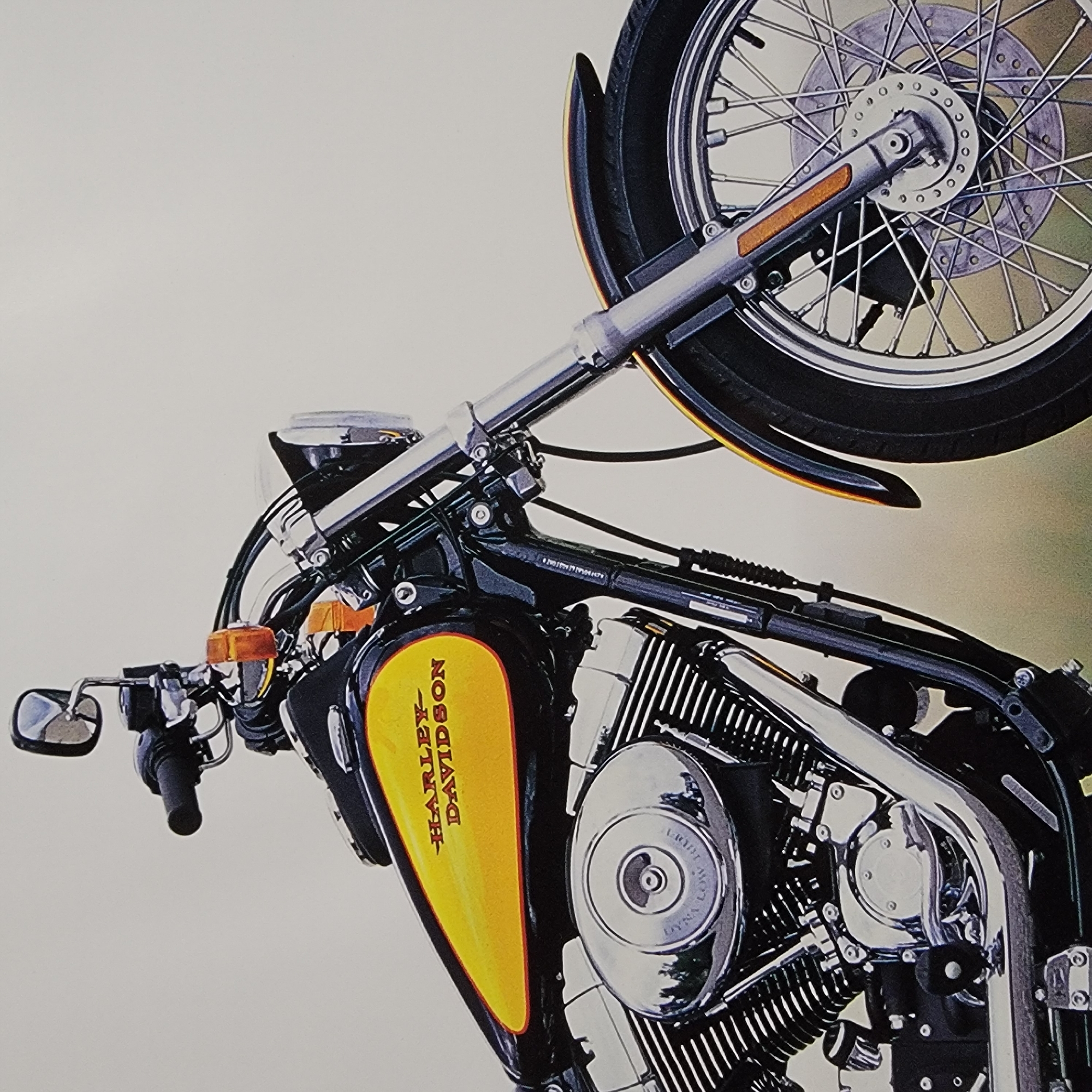 A Harley-Davidson motorcycle is positioned at a three-quarter view against a neutral, light-colored background. The motorcycle is predominantly black with vibrant yellow accents on its fuel tank, which is emblazoned with the "HARLEY-DAVIDSON" logo in orange. Key visible components include the handlebars with a mirror, a portion of the front suspension, the engine with chrome detailing and fins, the front wheel with spokes and a disc brake, and a section of the front fender. The overall impression is a studio-like product shot, with no city elements or environmental context visible, suggesting it is not located within a city.