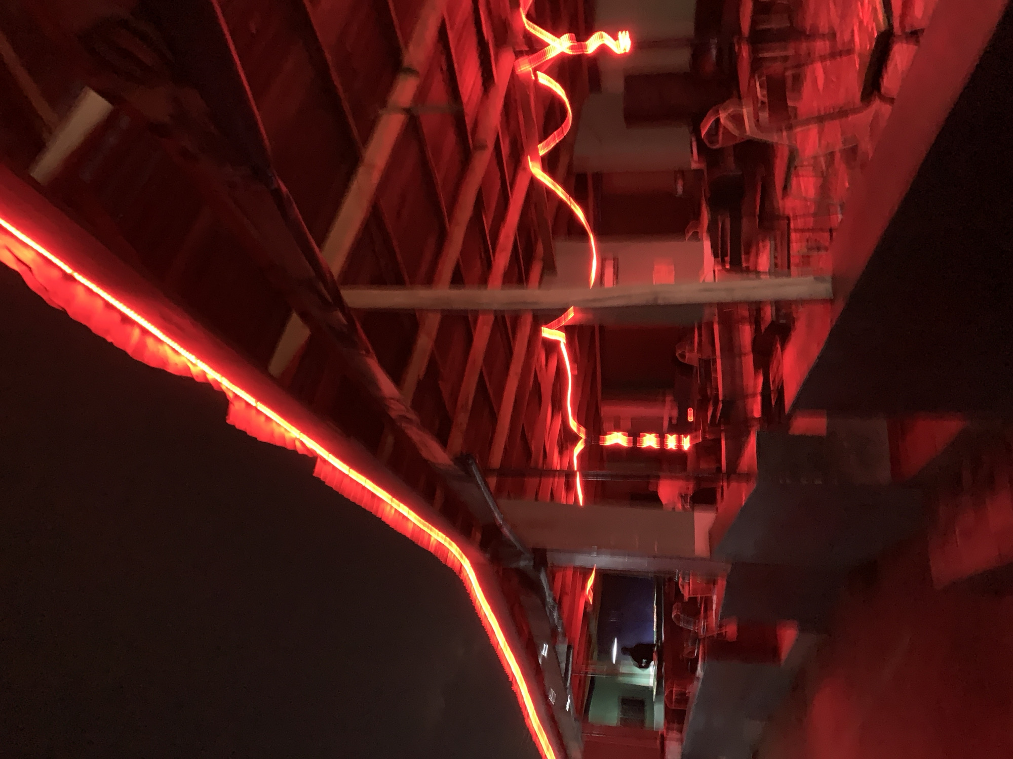 The image depicts an interior space illuminated with red lighting. The architecture suggests a building under construction or renovation, characterized by exposed beams and rafters in a sloped ceiling. Red LED strip lights are visible along some of the structural elements, accentuating the angles and lines. The overall environment is dark, with the red lights serving as the primary light source, which creates a strong contrast and a sense of enclosure.
Due to the lack of specific details and the ambiguity of the scene, it is impossible to definitively confirm if the image is located in New Stadium, Nigeria. The image does not contain identifiable markers specific to that city.