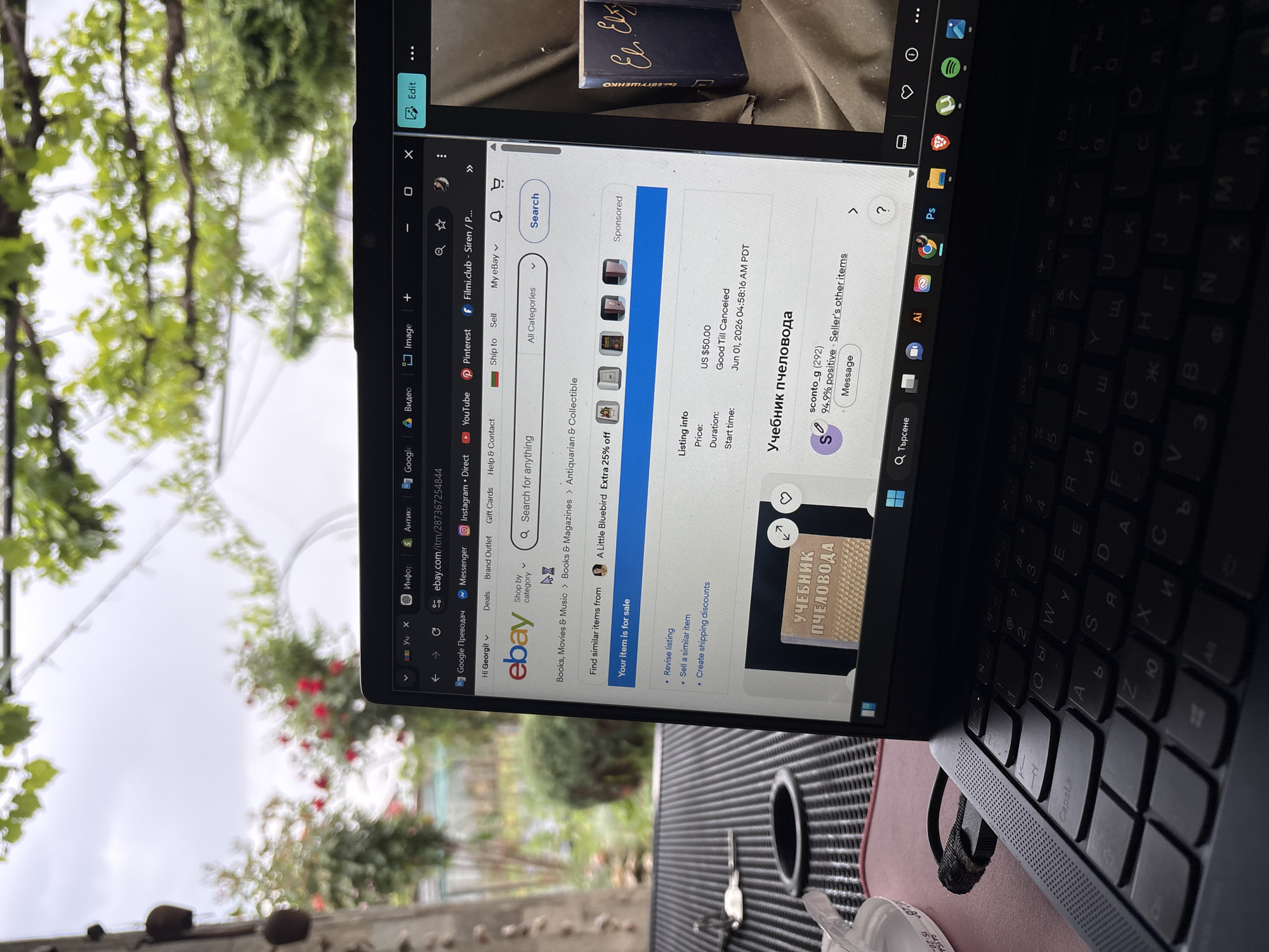 The image shows a laptop screen displaying an eBay page for an item titled "Учебник пчеловода" (Textbook of Beekeeping) in Russian, with a price of US $50.00. The laptop's keyboard is visible in the foreground. The background appears to be a view through a window, showing greenery, possibly a garden or trees. The screen also features shortcuts to websites like YouTube, Pinterest, and eBay. The city of Elin Pelin, Bulgaria, is not directly referenced or identifiable in the image.