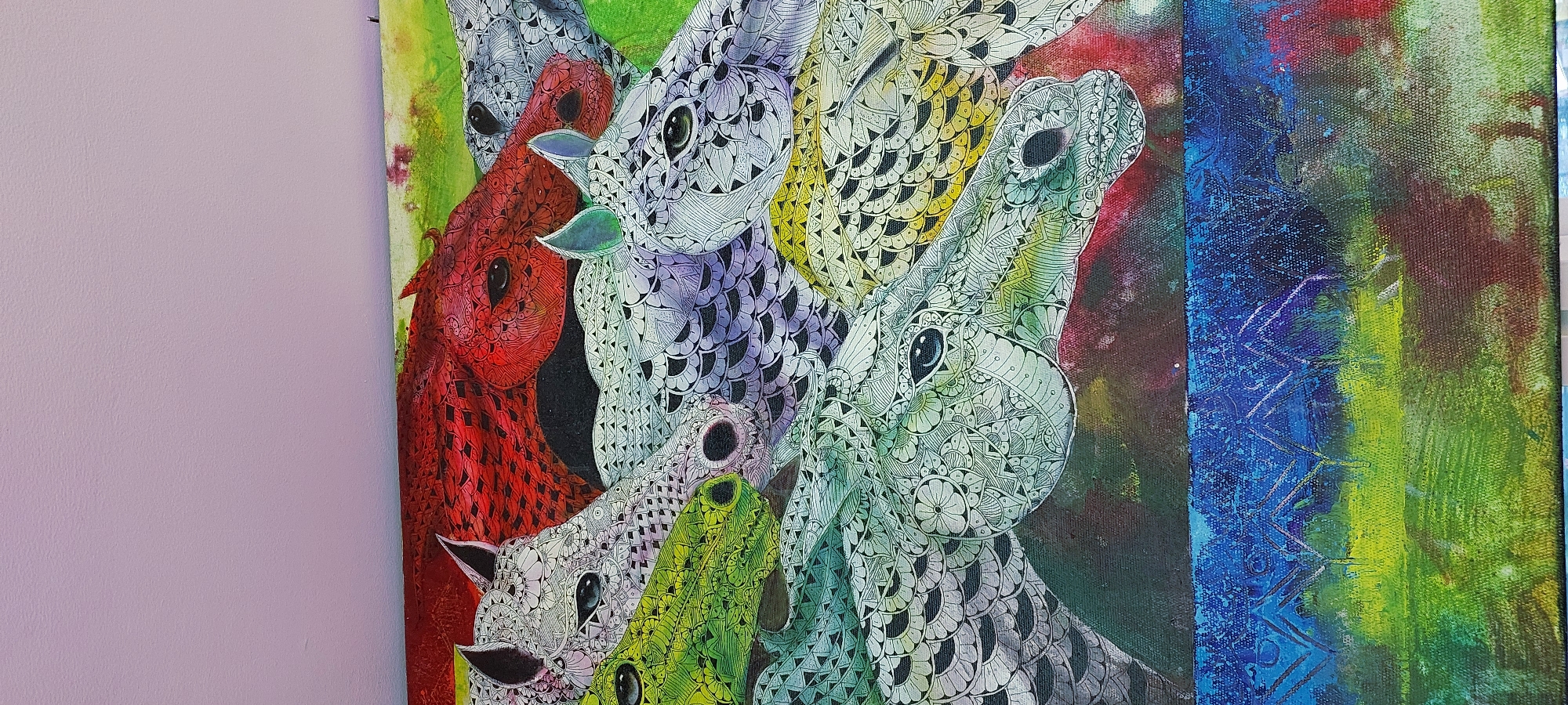 This is a close-up, top-down, eye-level shot of a colorful, textured painting of horses. The painting features several horse heads rendered in a detailed, intricate pattern of black and white linework, resembling zentangle art. The horse heads are depicted in various colors: one in red, one in green, one in purple, and one in yellow, layered and overlapping. The background of the painting is a blend of vibrant colors, including red, green, yellow, and blue, with abstract brushstrokes. The lower portion of the painting shows a distinct band of blue with white markings that appear to be abstract shapes or patterns, over a textured green and yellow base. The painting is displayed against a plain, light purple wall. The image does not depict any specific location in Curug Sangereng, Indonesia, as it is a close-up of artwork.
