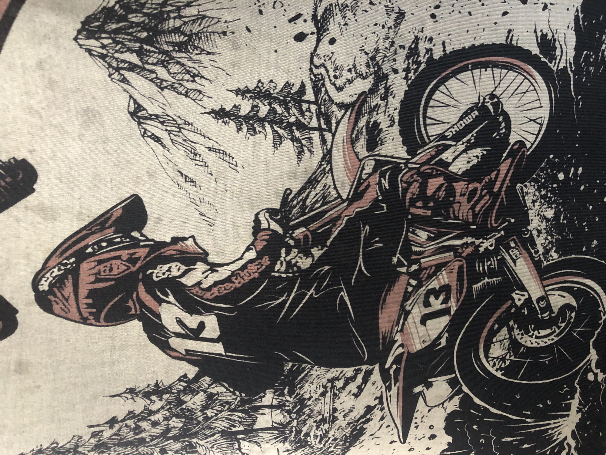 This image depicts a black and pink graphic on a light-colored fabric, likely a t-shirt. The graphic features a stylized illustration of a motocross rider on a dirt bike, set against a background of mountains and pine trees. The rider is wearing a helmet, racing suit, and boots, with the number "13" prominently displayed on the back of the suit and on the front of the bike. The dirt bike has intricate detailing, including spokes on the wheels and what appears to be a brand name "SHOWA" on the front suspension. The overall style is illustrative and somewhat gritty, with strong black lines and shading. The environment is depicted as rugged and natural, with a sense of movement implied by the dirt being kicked up around the wheels. There is no discernible location within the city of Пионерский, Russia, as this is a graphic illustration and not a photograph of a real-world scene.