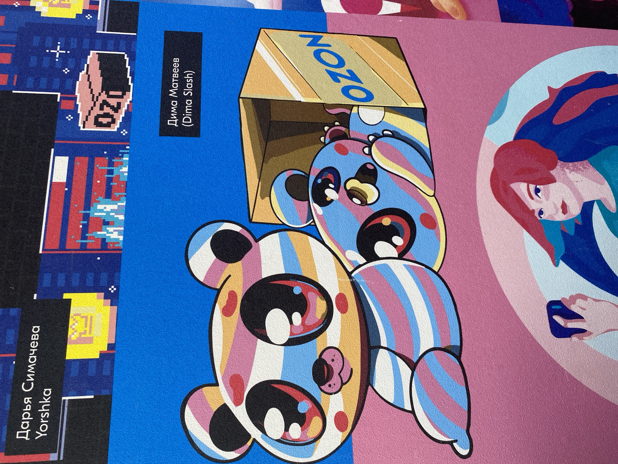 The image shows a wall with printed artwork. The left side features pixelated graphics with the Russian words "Дарья Симачева Yorshka" and "Дима Матвеев (Dima Slash)." The central image depicts two cartoonish bears with large eyes and striped patterns, one partially inside an "OZON"-branded cardboard box. The right side shows a stylized portrait of a person holding a smartphone. The artwork is likely located in Noviy, Russia, given the Russian text and the presence of OZON branding, which is a prominent Russian e-commerce company.