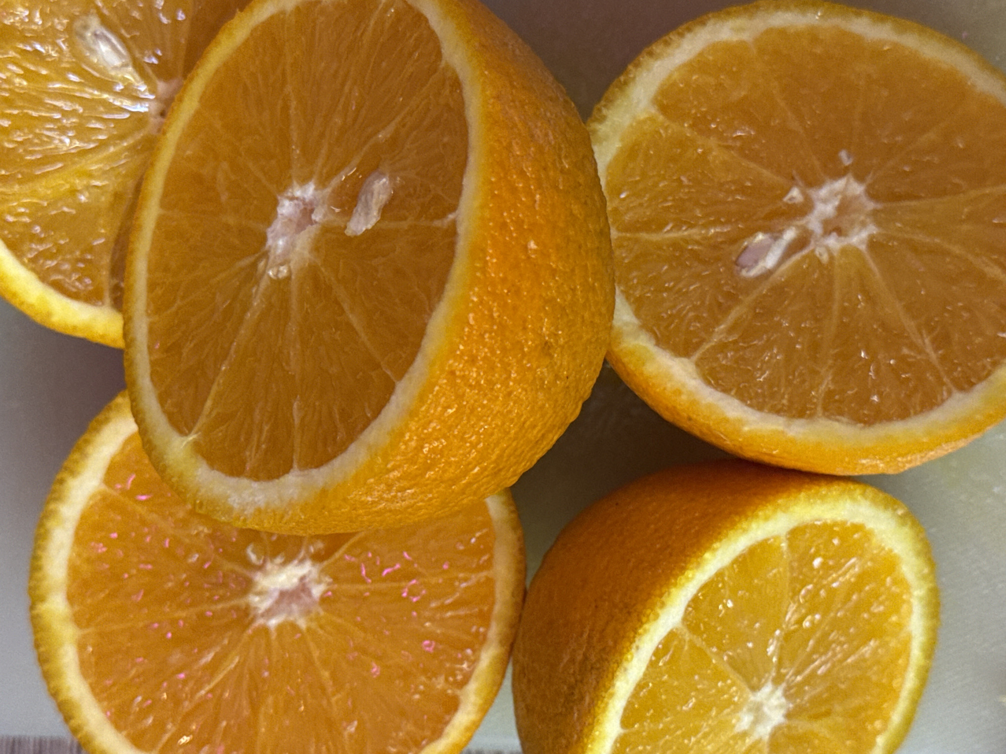 The image is a close-up, overhead shot of several sliced oranges. The oranges are bright orange and appear fresh, with visible segments and white pith. Some slices are whole, while others are halves. The lighting creates a slightly glossy effect on the fruit. There is no discernible background that would indicate a specific location in Moscow, Russia, or any other city. The composition is simple, focusing entirely on the texture and color of the citrus fruit.