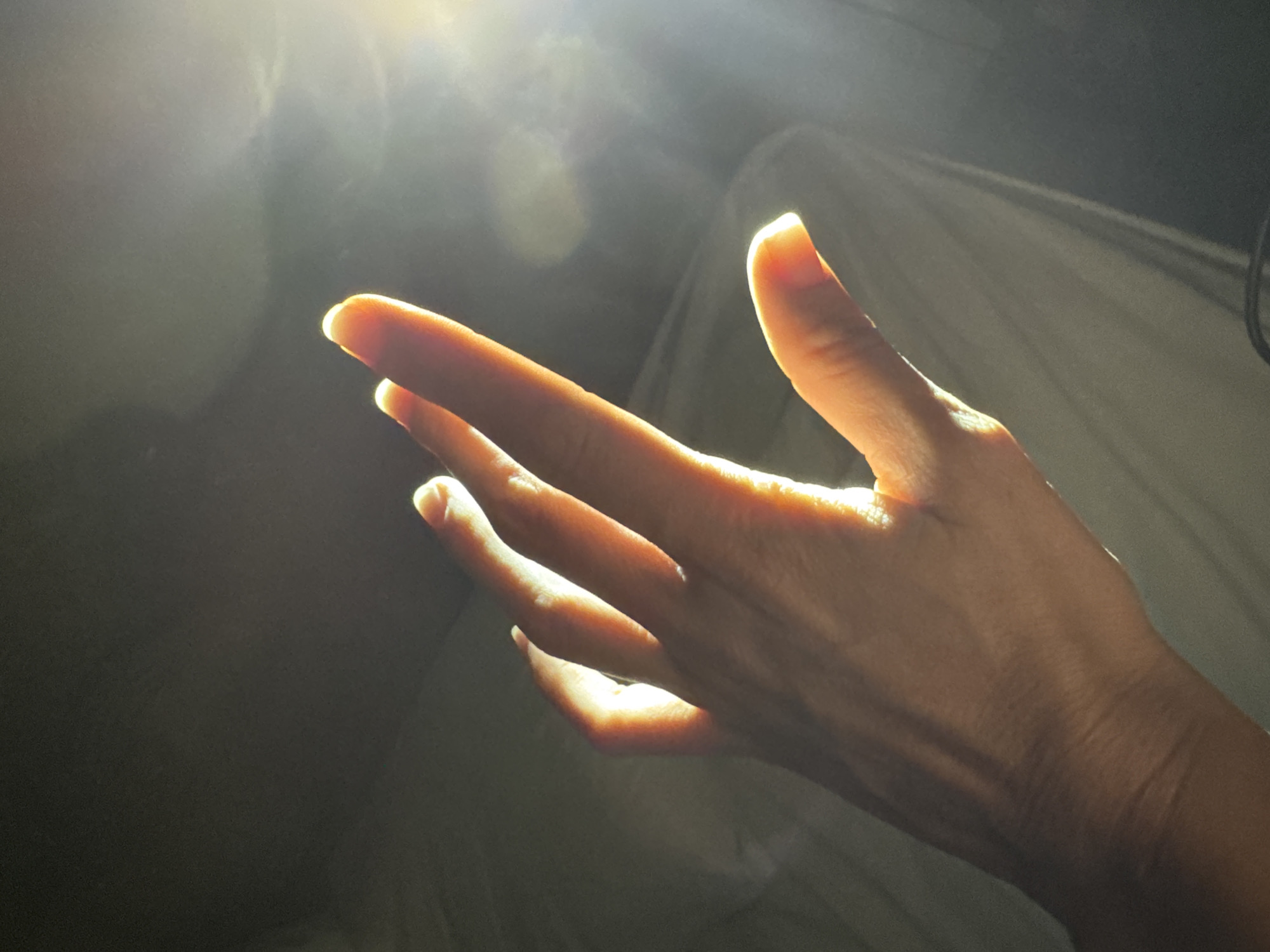 A hand is illuminated by a bright light source, with the fingers extended. The background is dark and out of focus, with some white fabric visible on the right side. The image does not contain enough information to place it definitively in Kuta Selatan, Indonesia, nor does it contain information on any actions or interactions taking place.