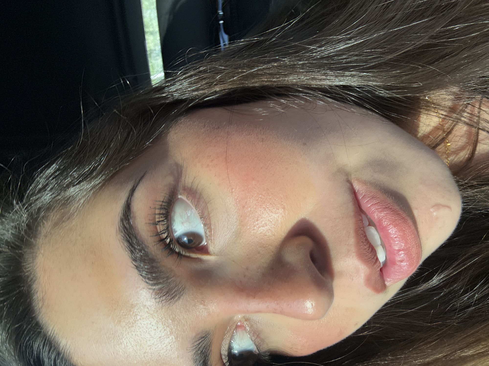 A close-up, slightly rotated portrait shows a person's face. The person has brown hair, fair skin, dark eyebrows, and brown eyes. The face is illuminated by sunlight. The location cannot be determined from the image. There are no discernible actions or interactions taking place. There is nothing else significant visible.
