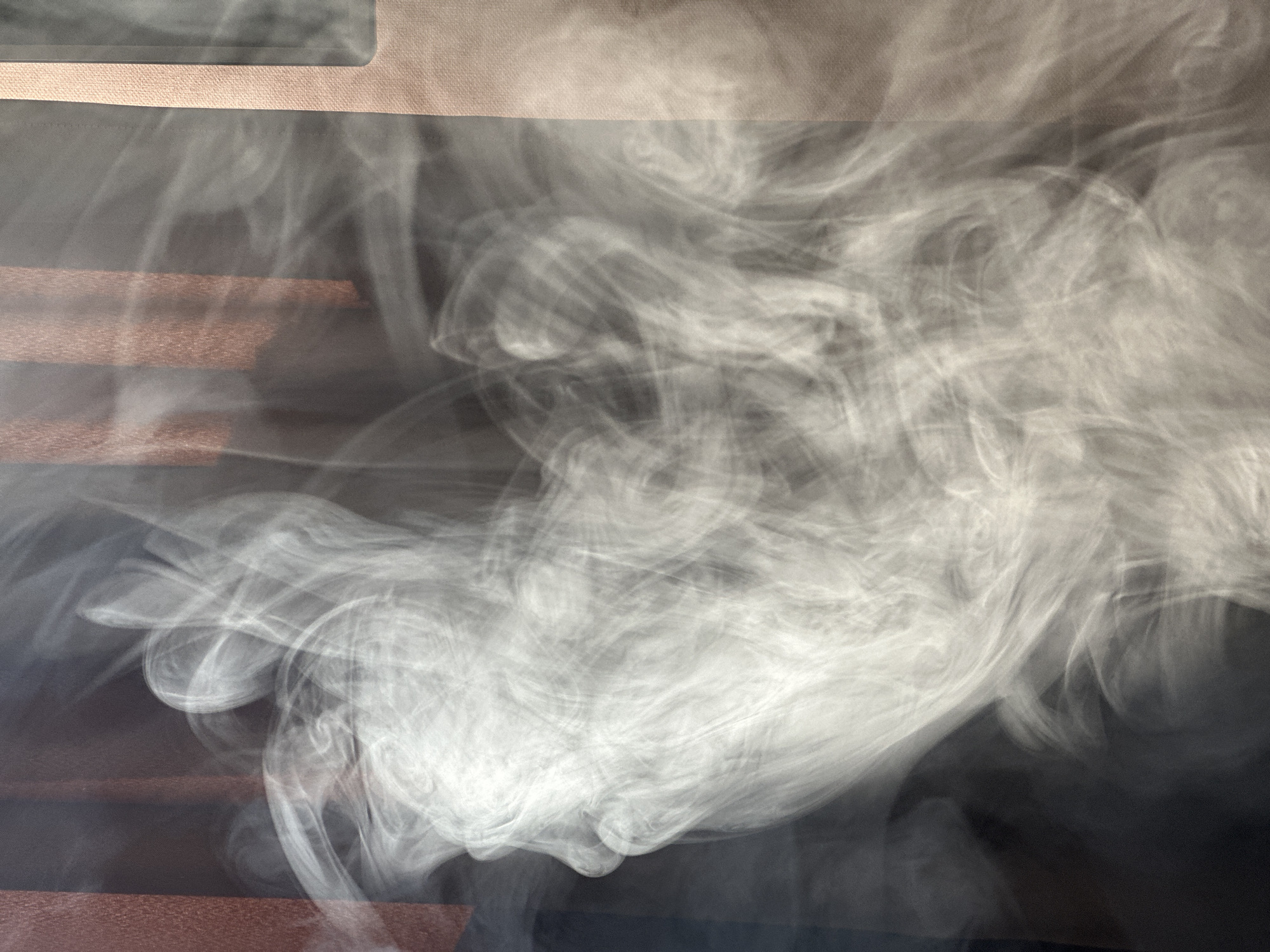 The image shows a dense plume of white smoke obscuring part of a dark, likely indoor scene. A textured, light-colored surface is visible near the top of the frame. Beneath, there are indistinct brown or reddish-brown horizontal bands. The smoke is thickest in the center and upper-right, with tendrils extending outwards. The location and city of Chaikovsky, Russia are not apparent from the visual content of the image.