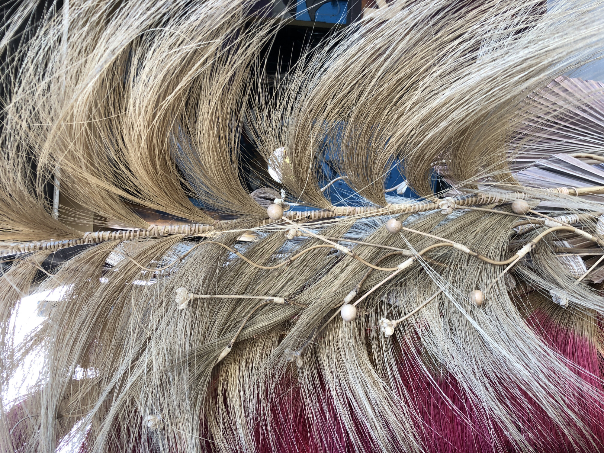 This media file is a close-up, eye-level shot of a decorative arrangement of dried grass and plant materials. The subjects are these natural elements, creating an intricate and textured display. The arrangement appears to be a form of naturalistic art or craft, possibly a garland, headdress, or a decorative element for a cultural event.
The materials are predominantly dried, straw-like grasses in shades of beige, light brown, and a subtle silvery-white at the tips. These are interwoven with thin, flexible twigs and possibly some sort of woven material, creating a layered and dynamic composition. Scattered throughout the arrangement are small, spherical, light-colored beads or seed pods, adding further detail and visual interest. Some delicate, dried flower-like formations are also present, attached to thin stems that weave through the grass. At the bottom of the frame, a vibrant, deep pink or magenta fabric provides a stark contrast to the natural tones of the grass, suggesting that this arrangement is placed upon or near this material.
The lighting appears to be bright and natural, possibly indicating daytime. There are no visible people, and the activity is the static display of the arranged materials. The setting is not clearly defined, but the presence of natural materials and the style of decoration might suggest a rural or culturally specific context. The overall mood is one of natural beauty and intricate craftsmanship. No visible text is present in the image. The location context provided is Keudekruenggeukueh, Indonesia, which aligns with the use of natural, possibly indigenous, plant materials in decorative arrangements.