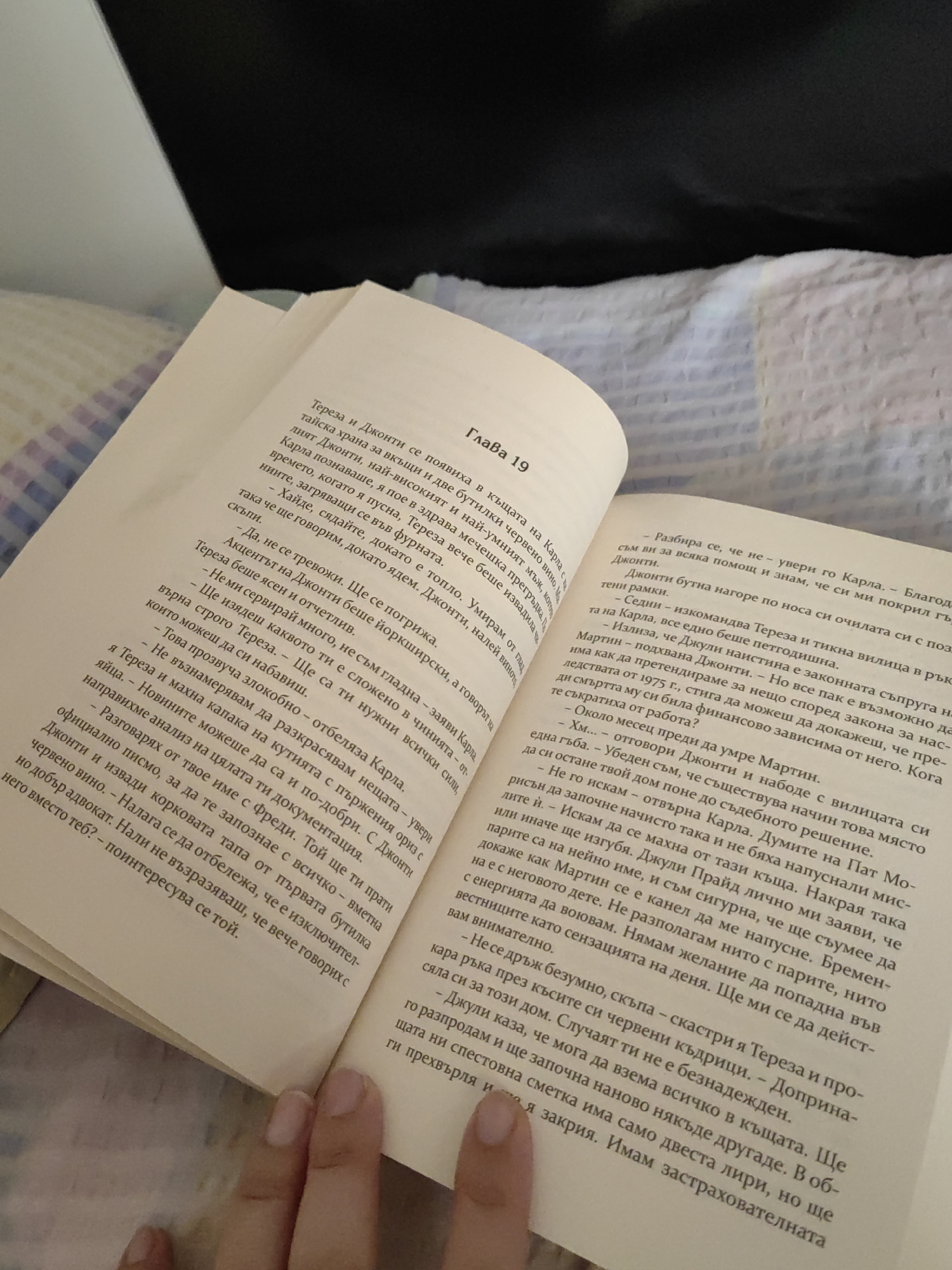 The image shows an open book with Bulgarian text. The text is in two columns, with the left column appearing to be a continuation of the right column. The book is placed on a white surface, possibly a bedspread with a subtle pattern. The lighting suggests an indoor environment. The book's pages are slightly bent, indicating it has been read. The text on the left page discusses Teresa and Djonti's appearance and their actions, mentioning a "chapter 19." The right page describes a conversation between Teresa and Djonti and their actions. There is no discernible connection to the city of Djerovo, Bulgaria, or any specific city within the provided image. The scene is a close-up of an open book, with a focus on the text and the pages.