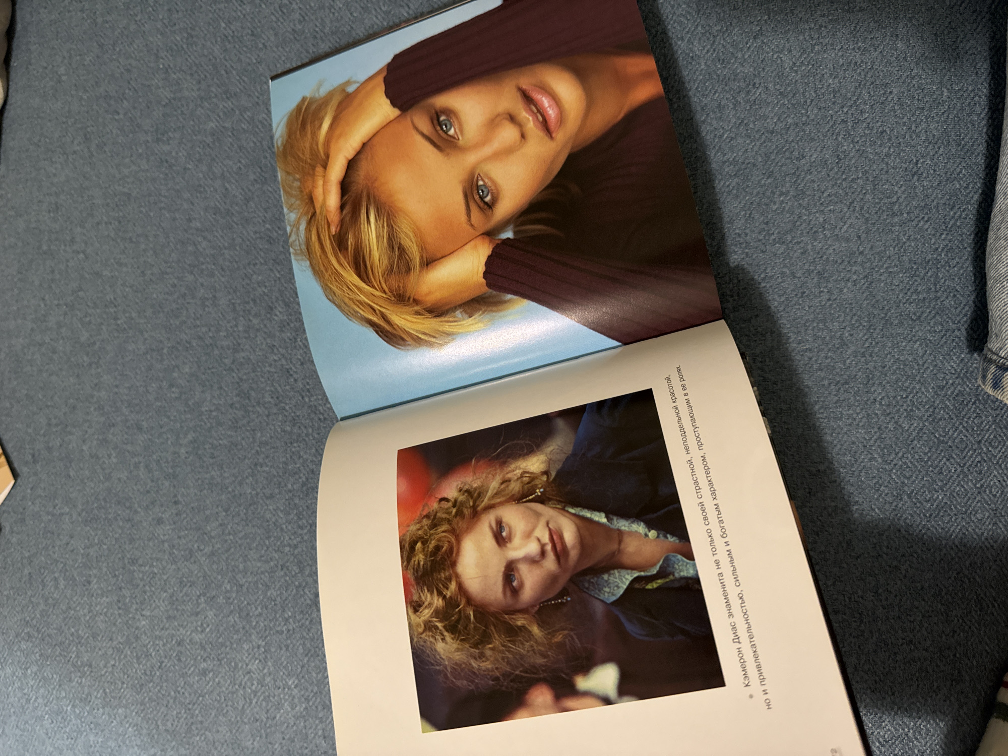 The image shows an open book with two pages visible. The top page features a close-up portrait of a blonde woman with light blue eyes, resting her head in her hands. The woman is fair-skinned and wears what appears to be a dark brown sweater. The background of the image is light blue. The bottom page features a picture of an older woman with curly blonde hair, wearing a dark blazer or jacket over a patterned top. The background is darker with some red tint. Some text in what appears to be Russian is visible on the lower page. The book is placed on a textured gray-blue surface.