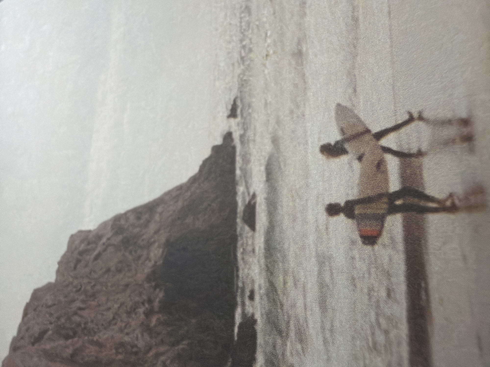 The image depicts two individuals walking on a beach, each carrying a surfboard. The scene is set against a backdrop of the ocean and a large, rocky cliff. The lighting suggests an overcast or hazy day. The individuals are silhouetted and appear to be walking away from the viewer, towards the water. The surf is visible in the mid-ground, with waves breaking near the shore. The overall atmosphere is one of tranquility and a connection with nature. The location is not in Kyiv, Ukraine.
