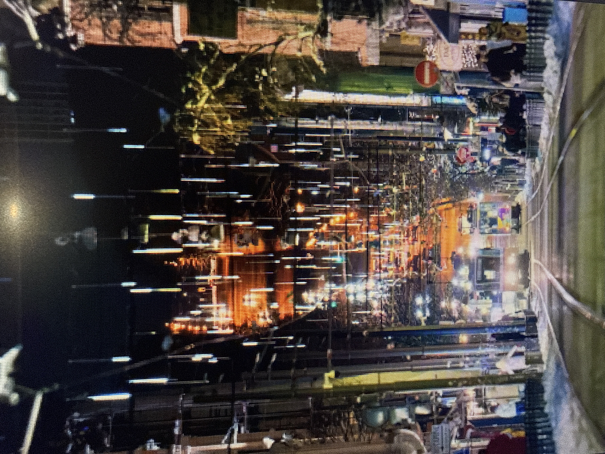 The image shows a street scene in Sofia, Bulgaria, likely taken at night. The street is illuminated by artificial lights, which appear as blurred streaks due to camera movement or a long exposure time. Buildings line the street, and some have illuminated windows. There are people walking on the sidewalk. A traffic sign is visible. The image quality is poor, with significant distortion and pixelation.