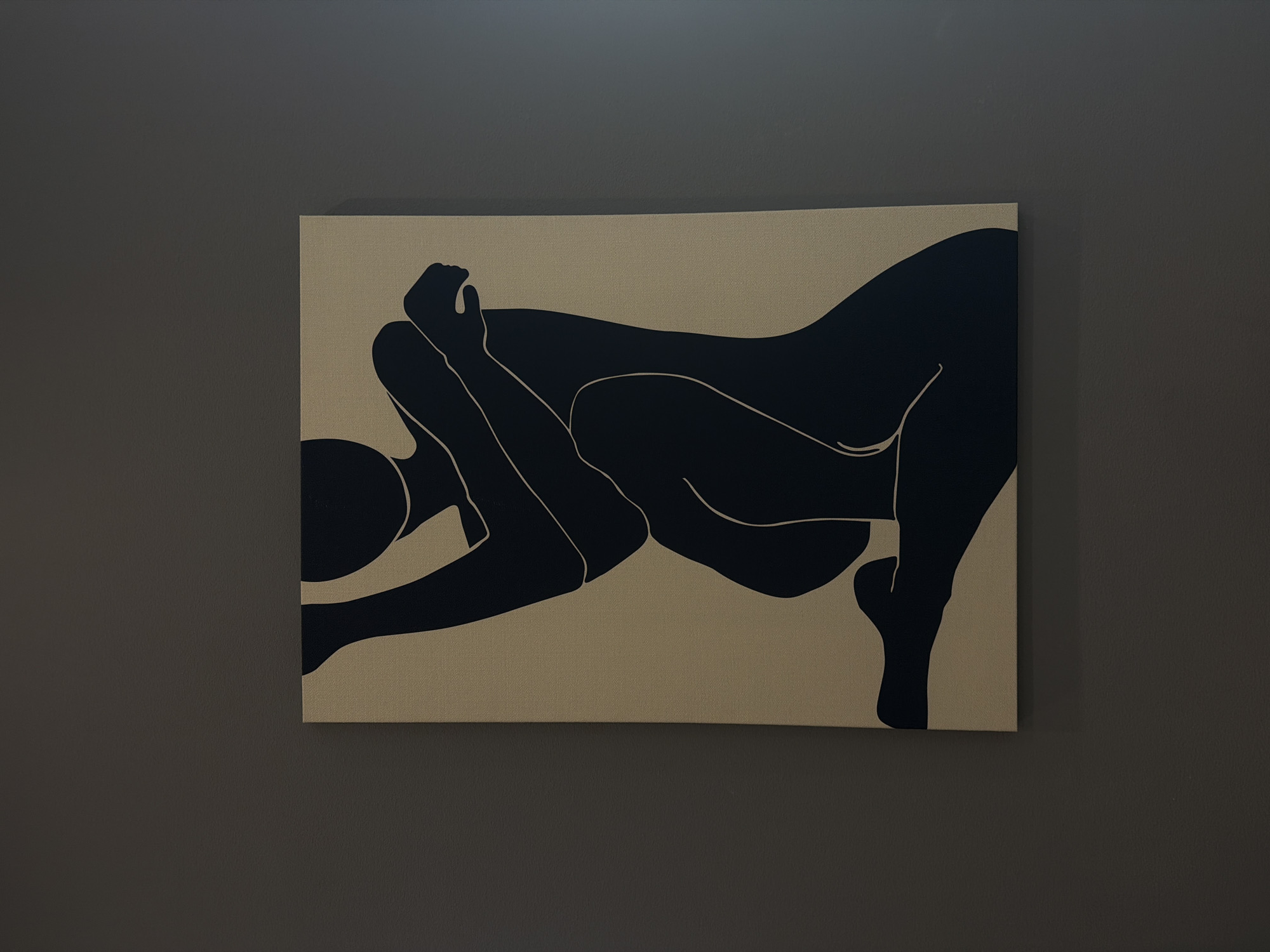 A framed canvas print hangs on a dark gray wall. The artwork depicts two figures in a modern, minimalist style. The figures are rendered in solid black against a tan or beige background. Their bodies are intertwined. The canvas is rectangular and appears to be hung evenly on the wall. The wall itself has a slightly textured surface. The location is Palm Desert, United States of America.