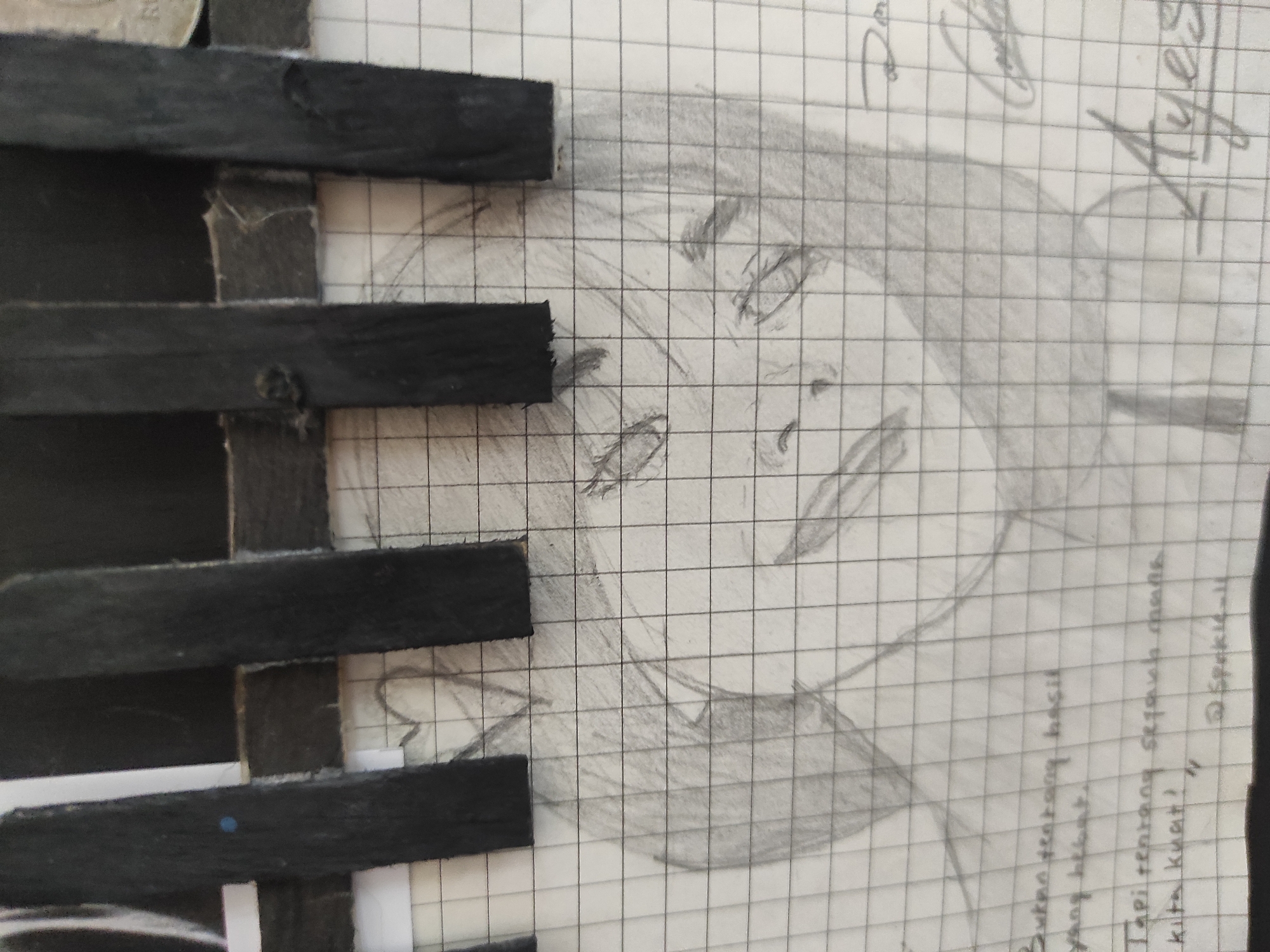 A close-up, eye-level shot features a grid-lined notebook with a pencil sketch of a person's face and some handwritten text. The sketch, drawn in monochrome pencil, shows a person with short hair, closed eyes, and a subtle smile. The facial features are soft and rounded. Above the sketch, four vertical black rectangular objects are positioned across the top of the image, creating a barred effect. These objects appear to be wooden sticks or similar rigid materials, some with visible textures and imperfections.
Below the sketch, handwritten text is visible. The first line reads, "Bukan tentang hasil". The second line appears to say, "yang hebat.". The third line states, "Tapi tentang segalah". The fourth line reads, "kita kuat!". Below this, there are some symbols and a username that reads "@Spokic-11".
On the right side of the image, partially obscured by the sketch and grid lines, are some scribbled signatures or artistic flourishes. One appears to be "Ayest". There is also some fainter text to the right of the sketch.
The overall impression is of a personal journal or art piece, possibly a creative work combining sketching and writing. The setting is not identifiable as a specific location in Sumedang, Indonesia, as the image focuses solely on the contents of the notebook.