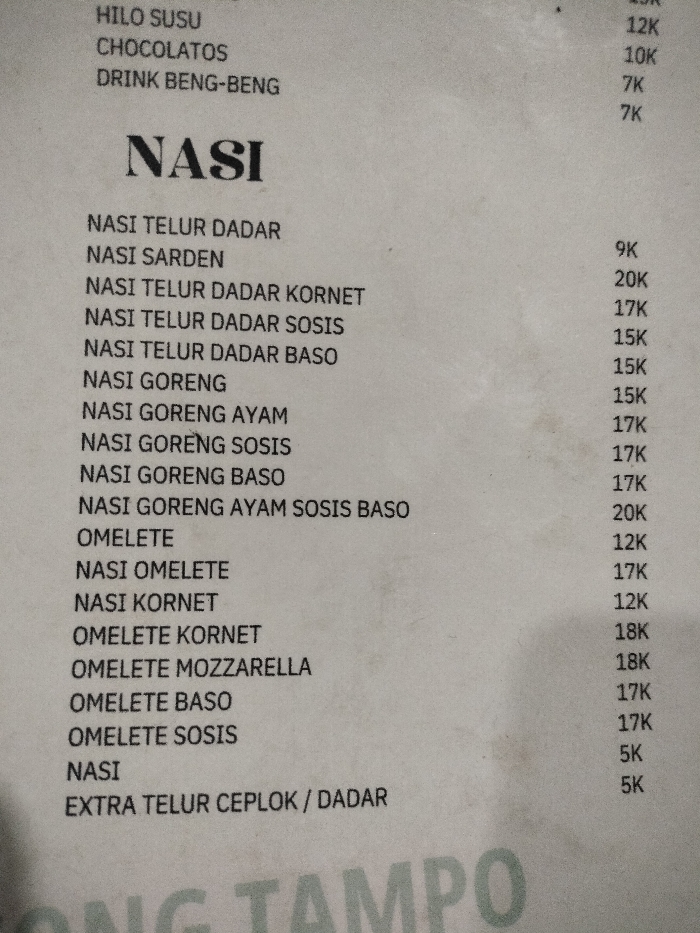 This media file is a photograph of a printed menu, likely from a casual eatery in Dramaga, Indonesia. The menu is printed on white paper with black text and appears slightly creased and aged. It lists various food and drink items with their corresponding prices.
The top visible section includes drinks:
- HILO SUSU (12K)
- CHOCOLATOS (10K)
- DRINK BENG-BENG (7K, followed by another 7K, suggesting two distinct "DRINK BENG-BENG" options or a repeat).
The main section, prominently titled "NASI," lists rice-based dishes:
- NASI TELUR DADAR (9K)
- NASI SARDEN (no price visibly associated)
- NASI TELUR DADAR KORNET (20K)
- NASI TELUR DADAR SOSIS (17K)
- NASI TELUR DADAR BASO (15K)
- NASI GORENG (15K)
- NASI GORENG AYAM (15K)
- NASI GORENG SOSIS (17K)
- NASI GORENG BASO (17K)
- NASI GORENG AYAM SOSIS BASO (20K)
Following the "NASI" section, there are omelette and other rice-related items:
- OMELETE (12K)
- NASI OMELETE (17K)
- NASI KORNET (12K)
- OMELETE KORNET (18K)
- OMELETE MOZZARELLA (18K)
- OMELETE BASO (17K)
- OMELETE SOSIS (17K)
- NASI (5K, likely plain rice)
- EXTRA TELUR CEPLOK / DADAR (5K)
The prices are indicated with "K," which typically stands for thousands (Rupiah) in Indonesia, aligning with the location context. Part of a larger text, "ONG TAMPO," is visible at the very bottom of the menu. No activity or specific time of day is discernible from the image.