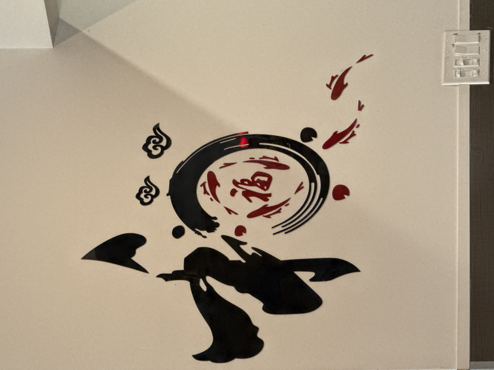 The image shows a wall in Darien, United States of America, adorned with black and red decorative wall stickers. These stickers depict Chinese-inspired artwork, including stylized fish, clouds, and abstract shapes. A light switch is visible near the right edge of the wall.