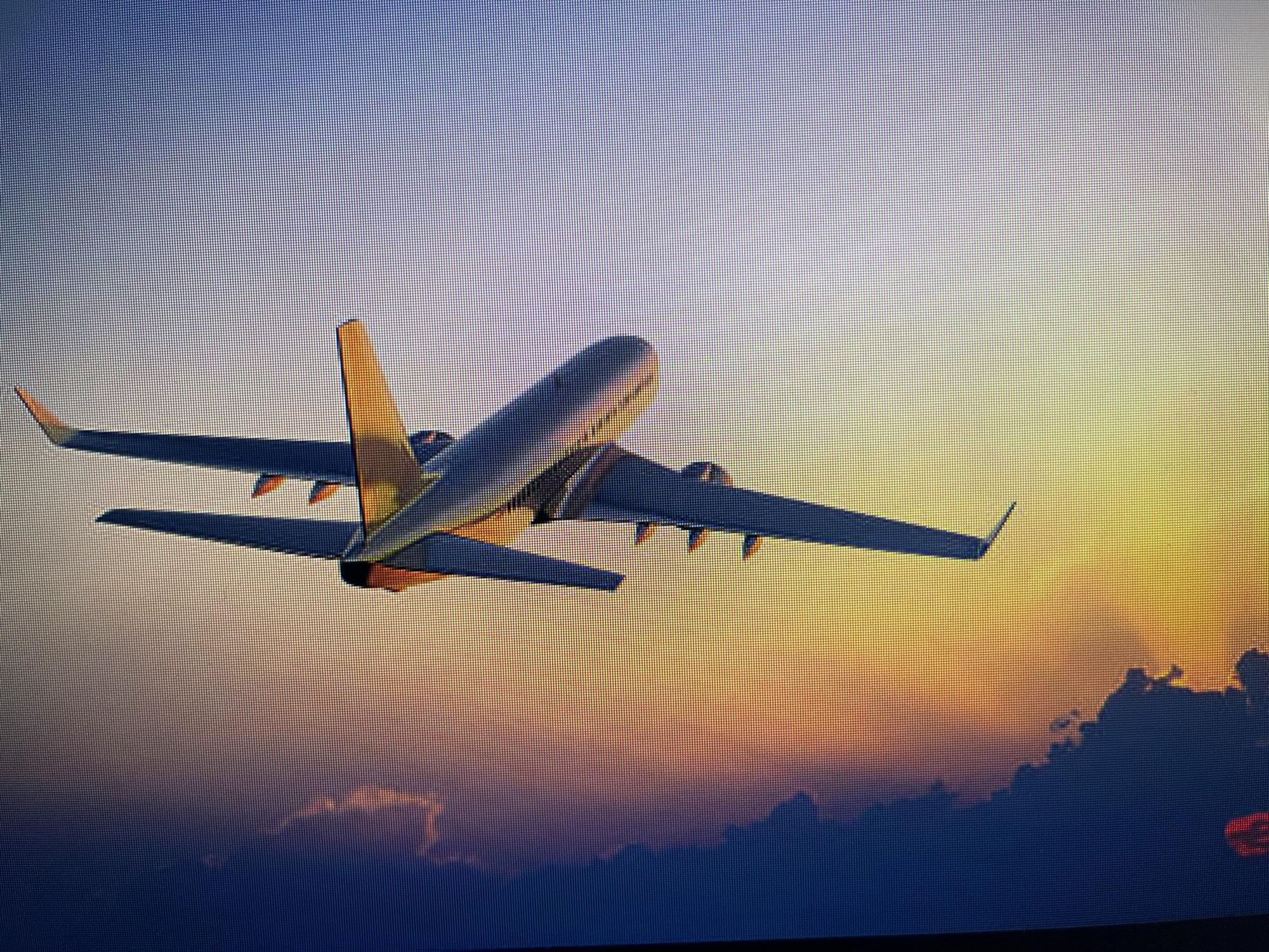 A commercial passenger airplane is in flight at sunset or sunrise. The airplane has two engines mounted under each wing. Below the airplane is a layer of clouds. The sky transitions from blue at the top to yellow and orange near the horizon. The location is unidentifiable; there is no way to determine if the location is Varna, Bulgaria.