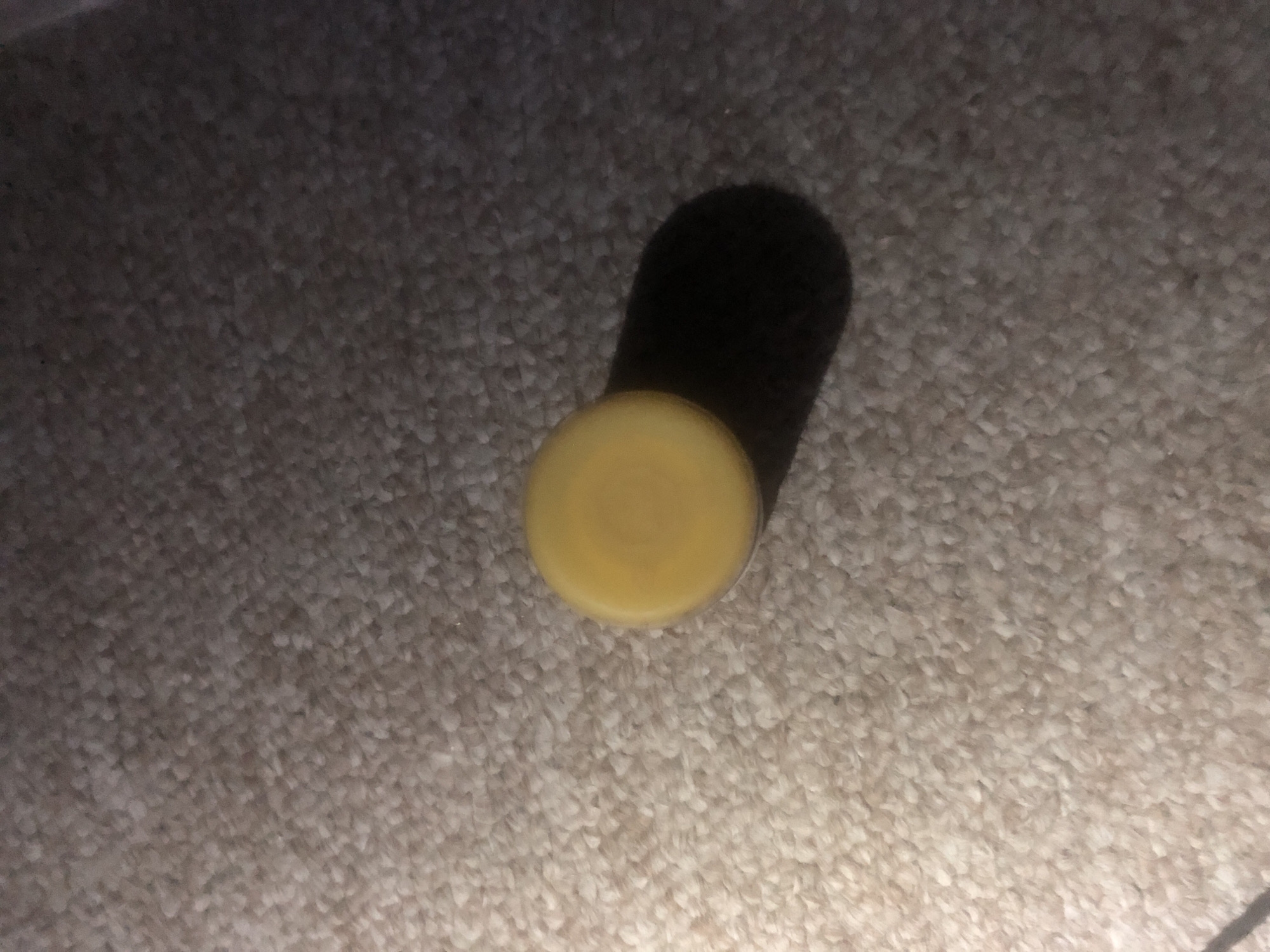 A small, round, yellow object is resting on a beige carpeted surface. The object casts a dark shadow to its right. The lighting in the image is uneven, with a bright light source illuminating the top left portion of the scene and casting the right side into shadow. There are no people or other discernible objects in the image. The scene is domestic and appears to be indoors. There is no information about the location in Jalingo, Nigeria.
