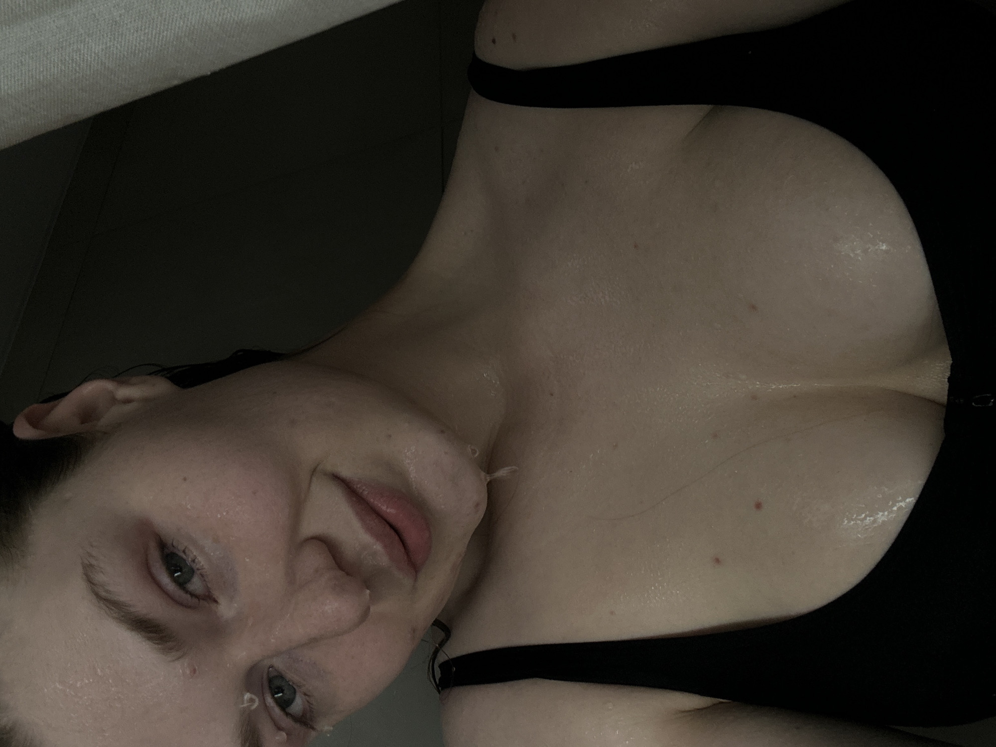 A close-up, angled portrait of a fair-skinned woman wearing a black tank top. Her skin is damp, possibly with sweat or water droplets visible on her face and chest. Her hair is dark and appears wet. She has light-colored eyes and is looking towards the viewer. The background is dark and indistinct. There is no information available to suggest the image was taken in Kazan, Russia.