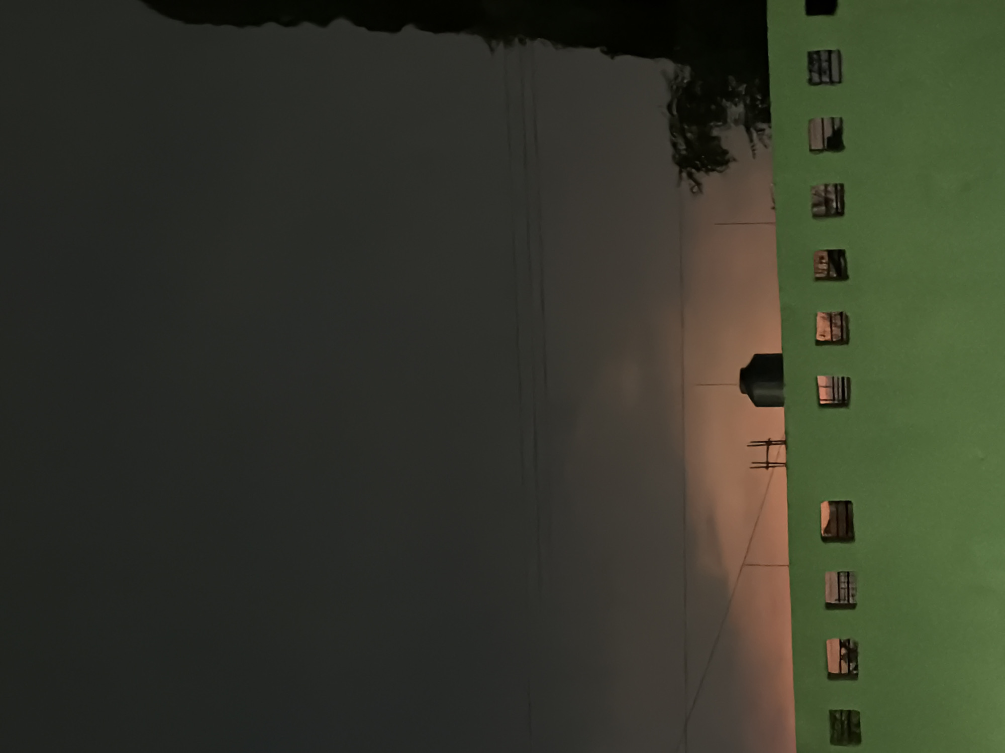 The image depicts a nighttime scene in Cuautla, Mexico. A green building with a series of square windows dominates the right side of the frame. A water tank is visible near the building, along with electrical lines. The background features a dark expanse, possibly water or sky. No people are visible.