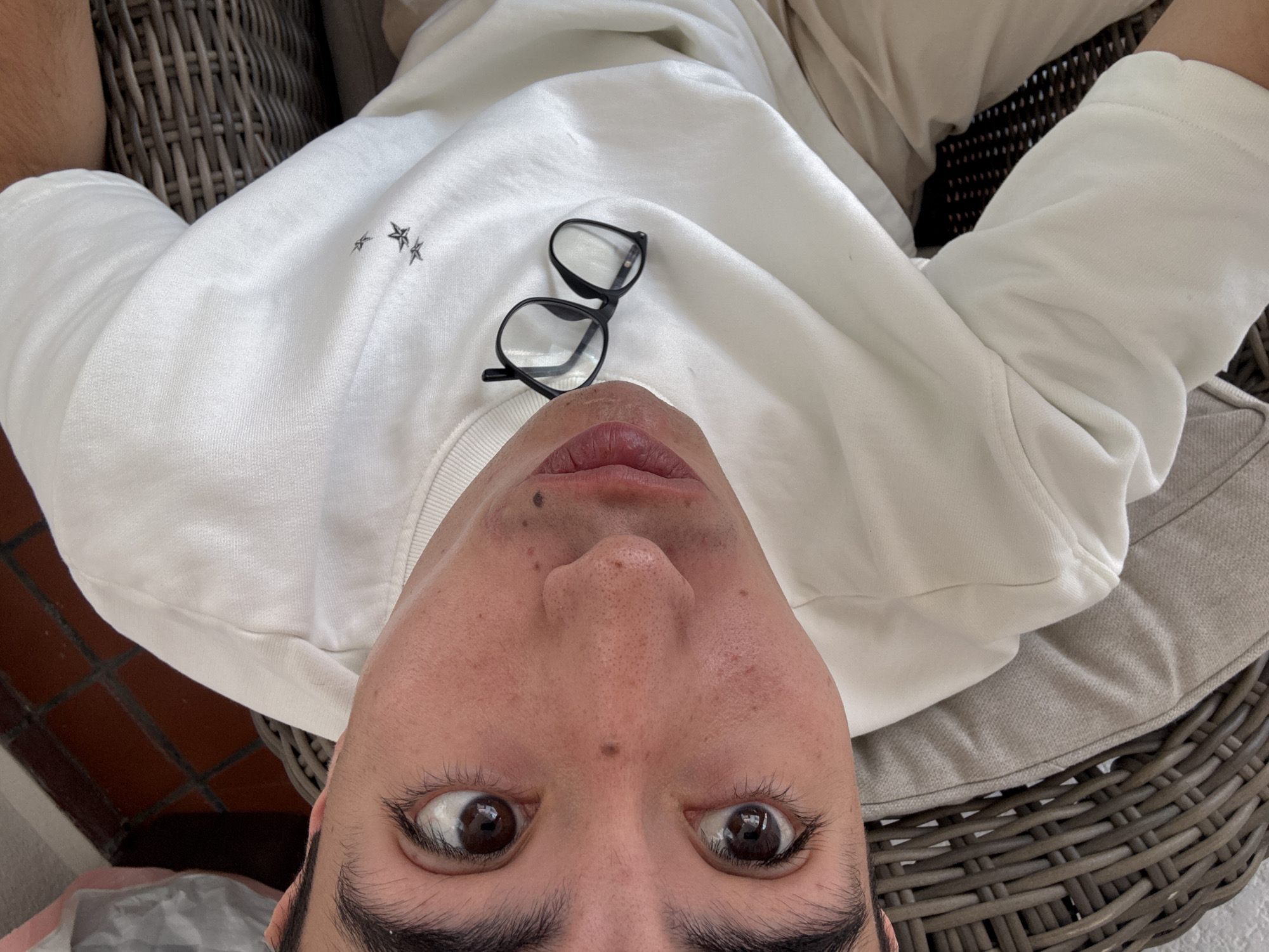 A man lies on a wicker chair. He wears a white sweatshirt. A pair of black glasses rests on the sweatshirt above his face. He appears to be in Puebla, Mexico, though the specific location is not discernible from the image.